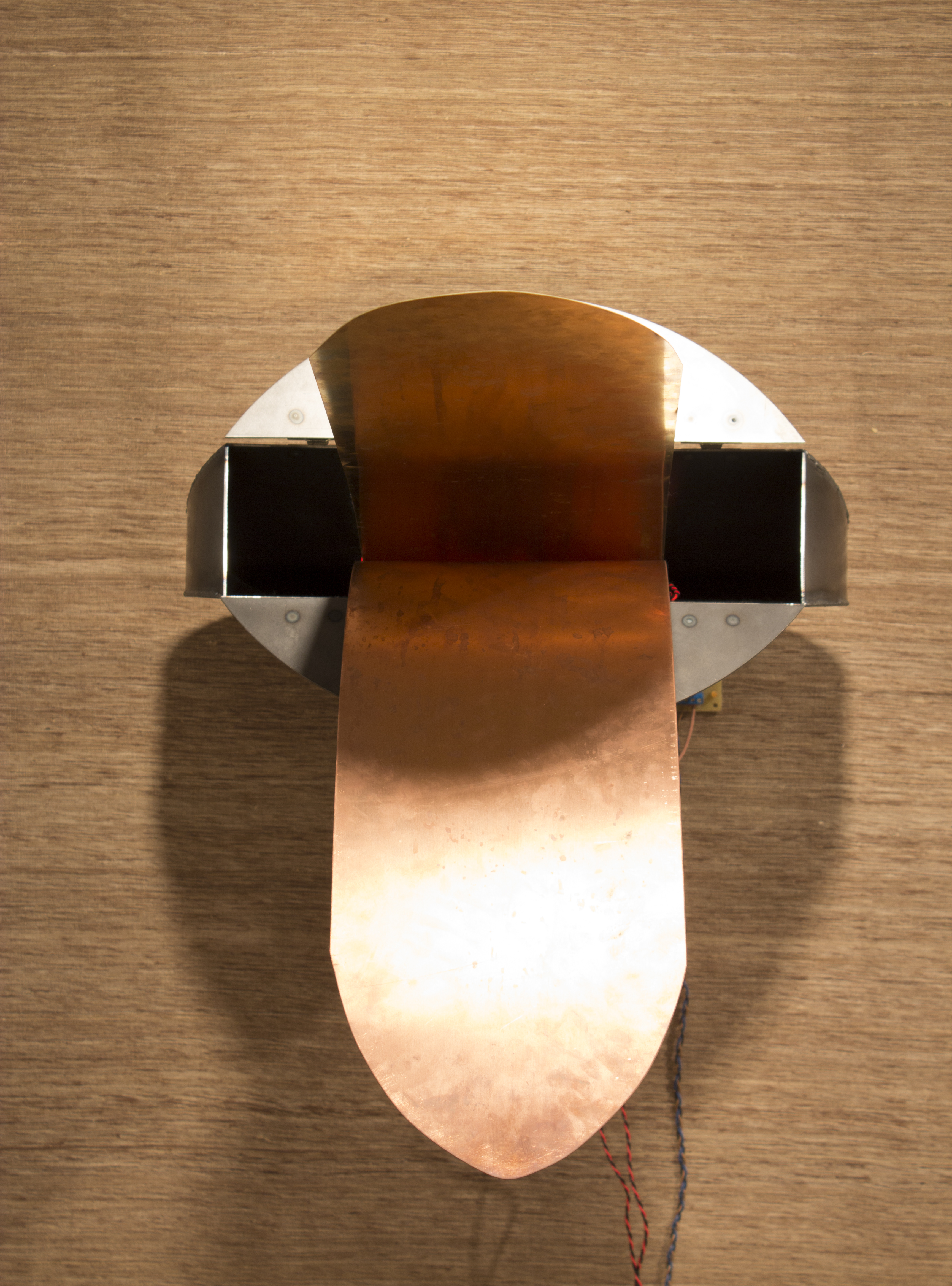 Two bronze strips extend from a rectangle metal box with open flaps, giving the appearance of a duck bill. Wires hang below.
