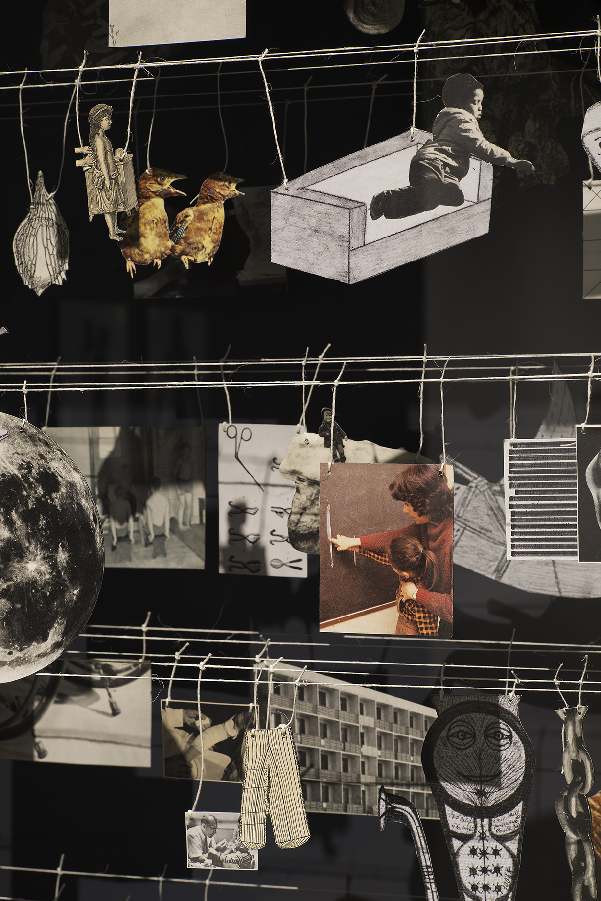 Many small two dimensional objects, including photos and drawings, hang from strings on a clothesline-like structure.