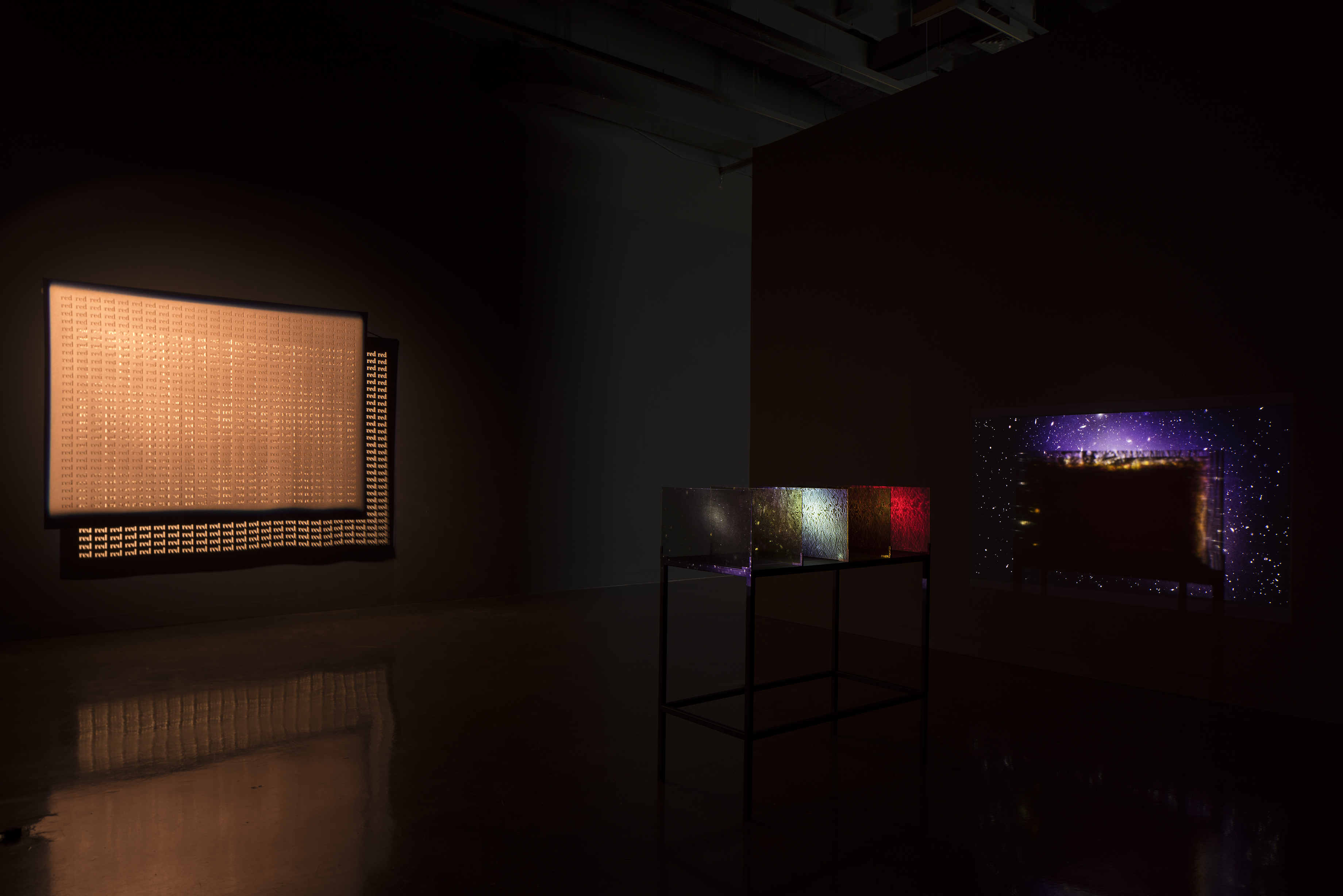 Lit orange screen hangs next to the colorful projection of stars and orbs through the glass panels of a table sculpture.