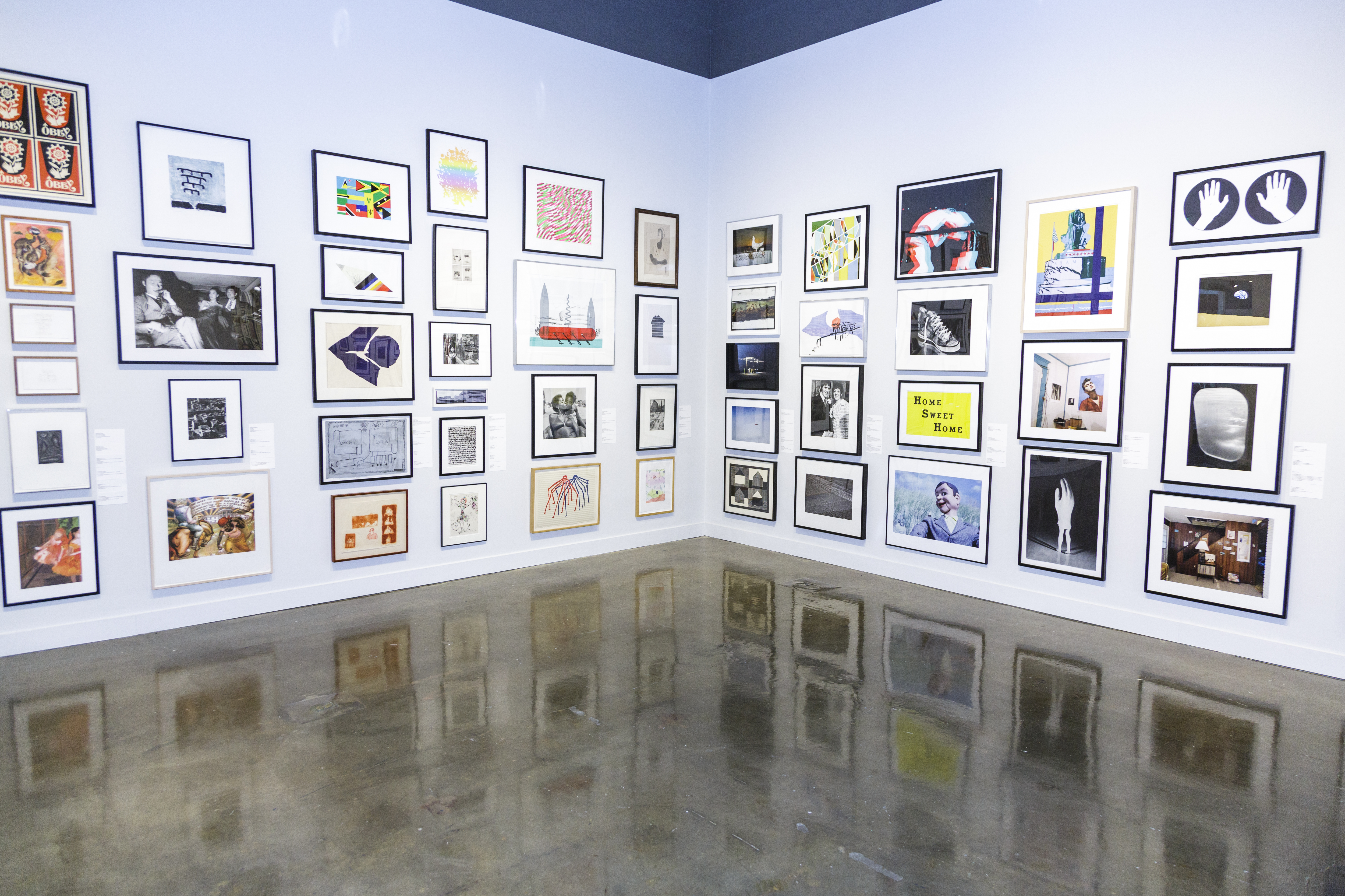 Corner of a gallery with small works of art hung salon style floor to ceiling.