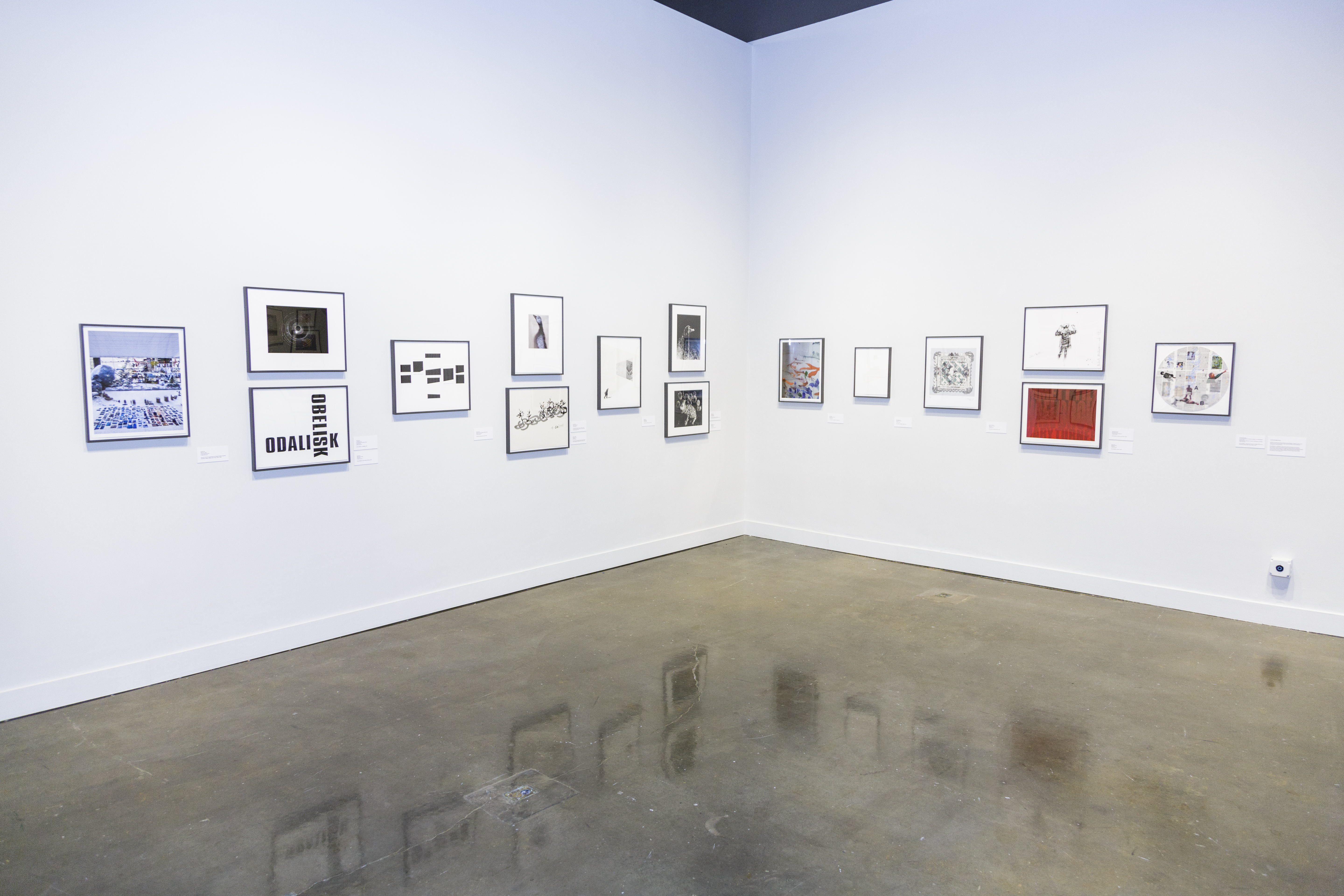 Corner of a gallery with small works of art hung salon style floor to ceiling.