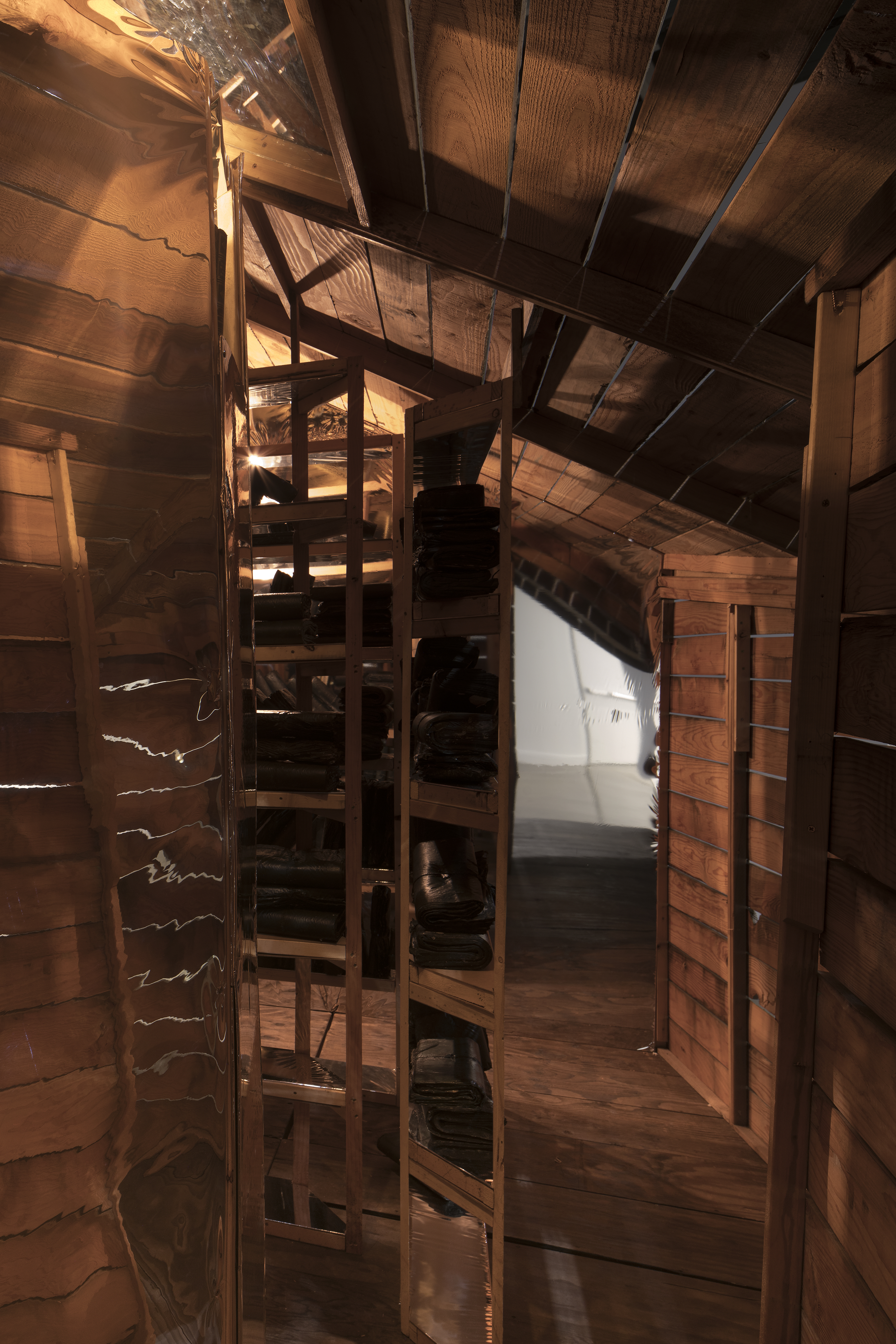 A view from inside an attic like space with dark wood planks, a slanted ceiling, lights and a doorway slanted at the top