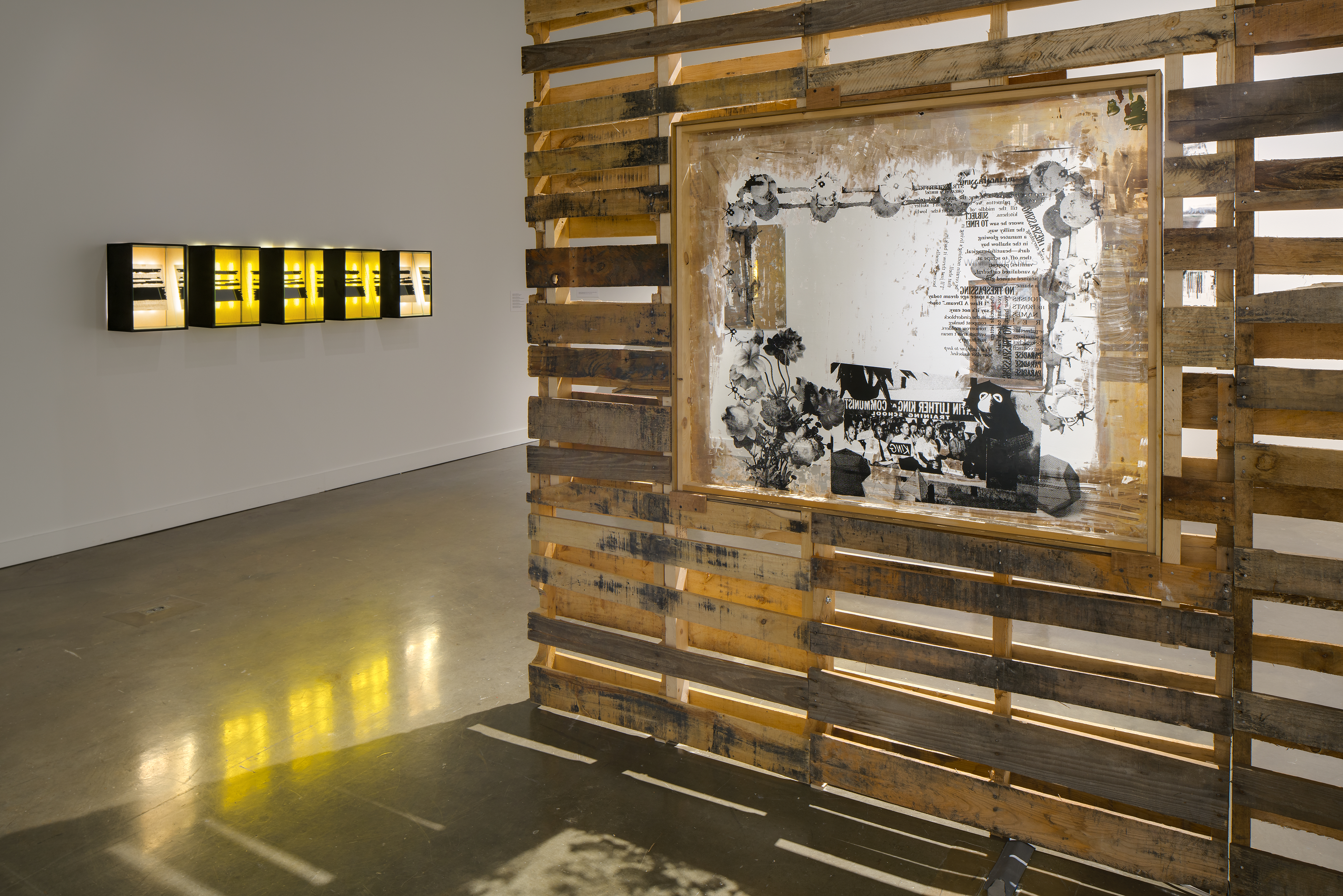 A wood slatted wall with a framed picture on the right, and five dark framed     boxes in a row, lit from within, on the far wall