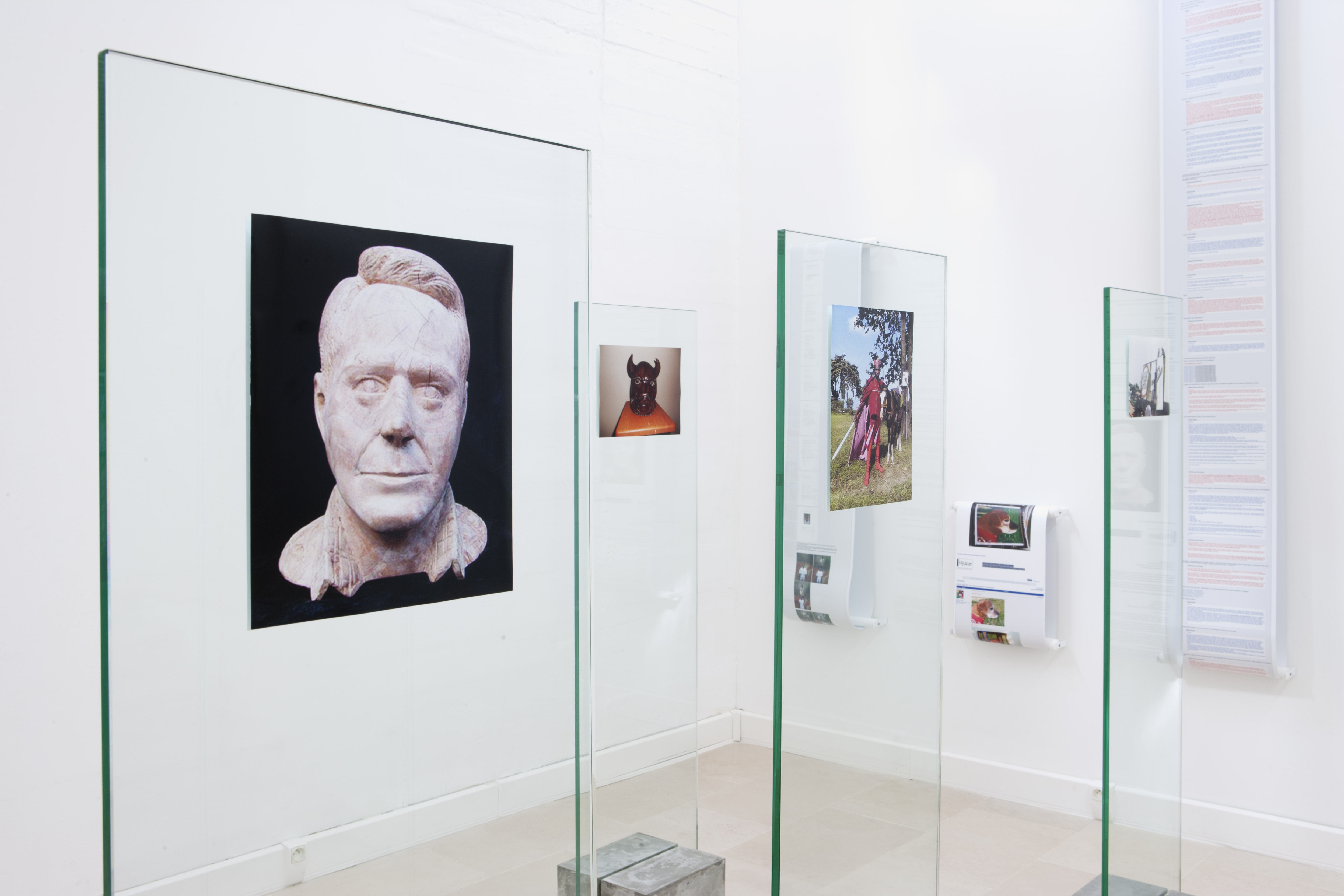 In the foreground, photographs mounted on glass panels, on the back wall, photos and text on rolls hang vertically.