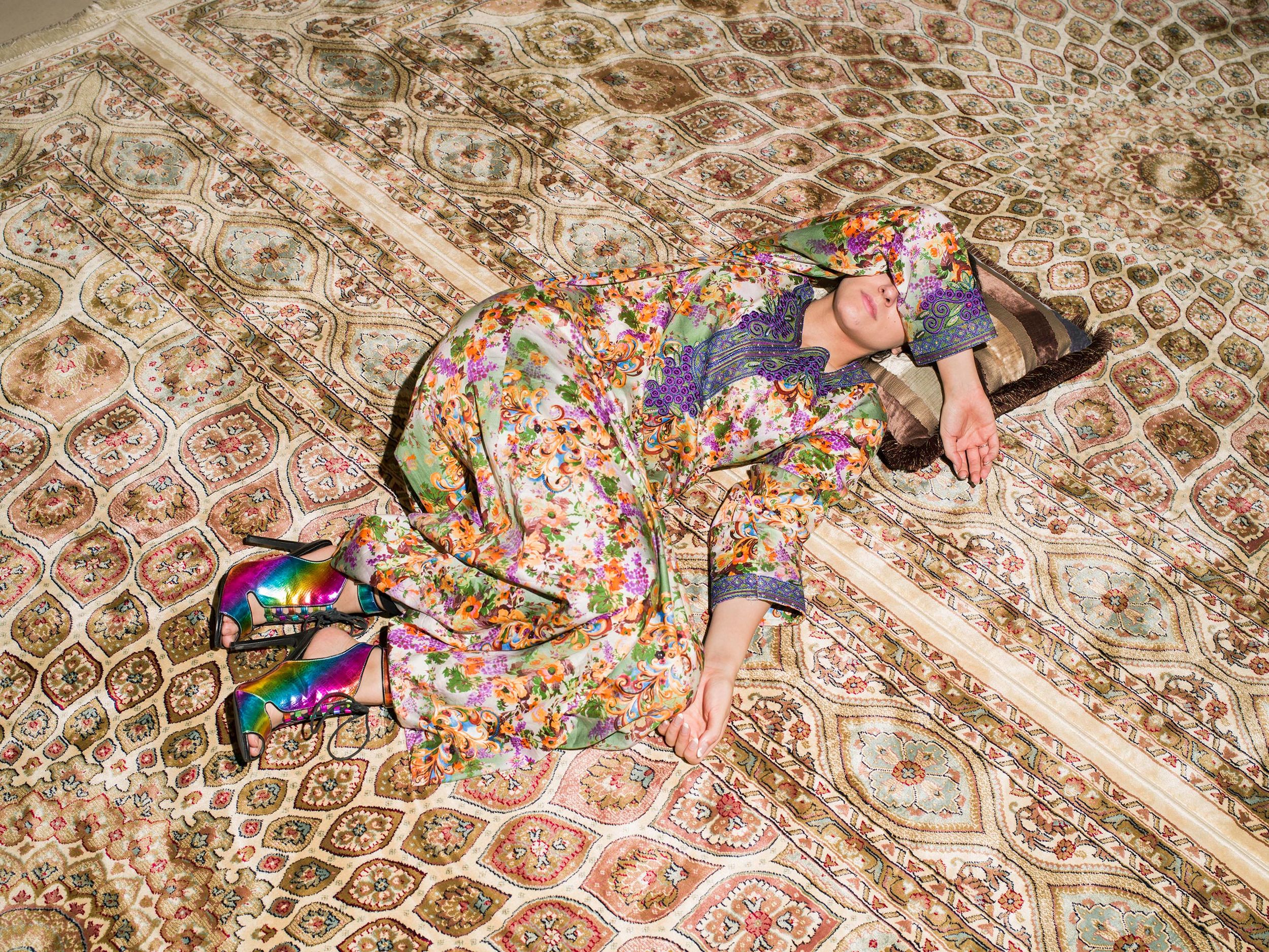 A body is curled up and camoflauging with a colorful carpet.