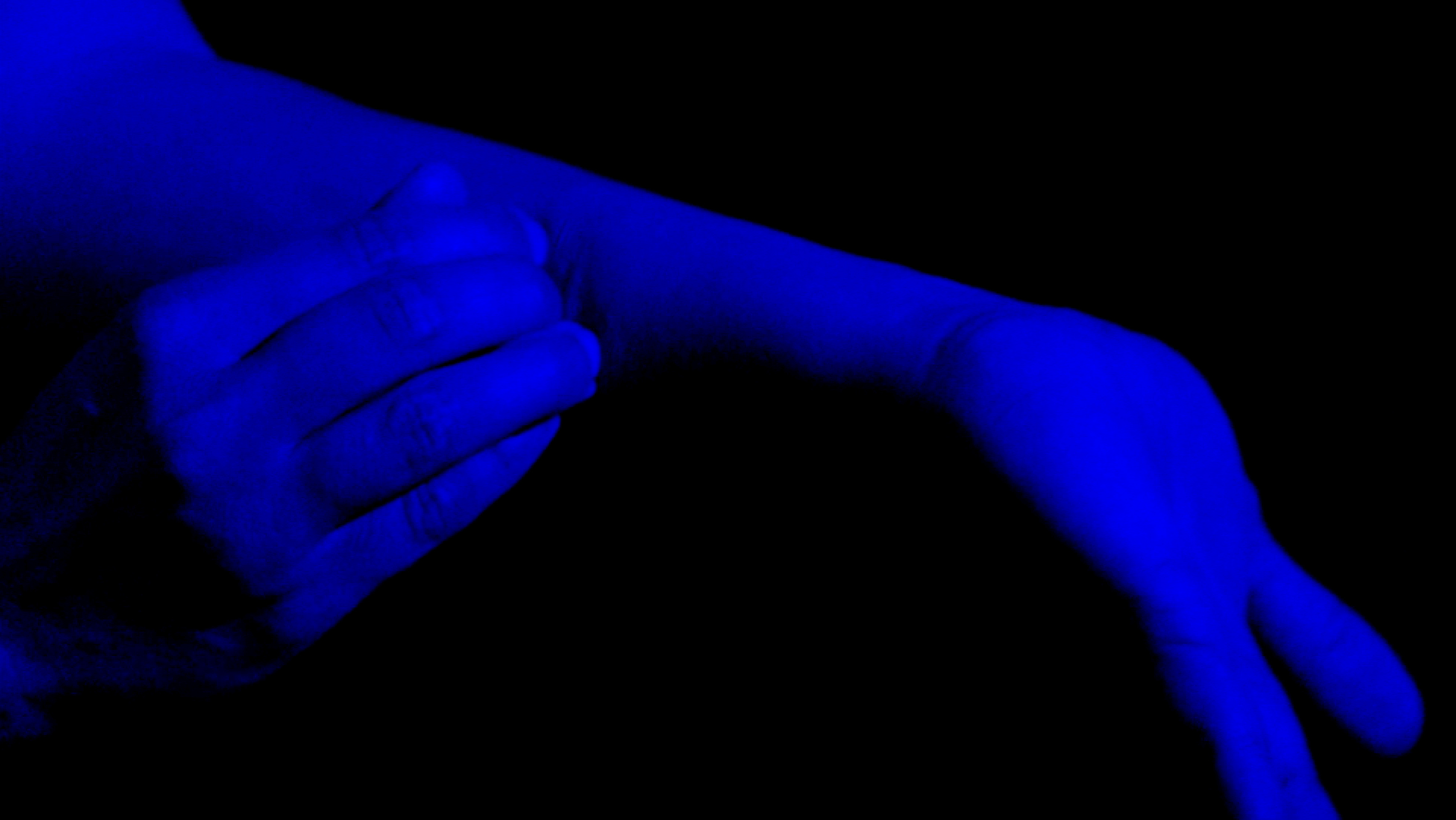 Blue colors the image of a right hand touching part of the left arm with flexed left hand against a black background.