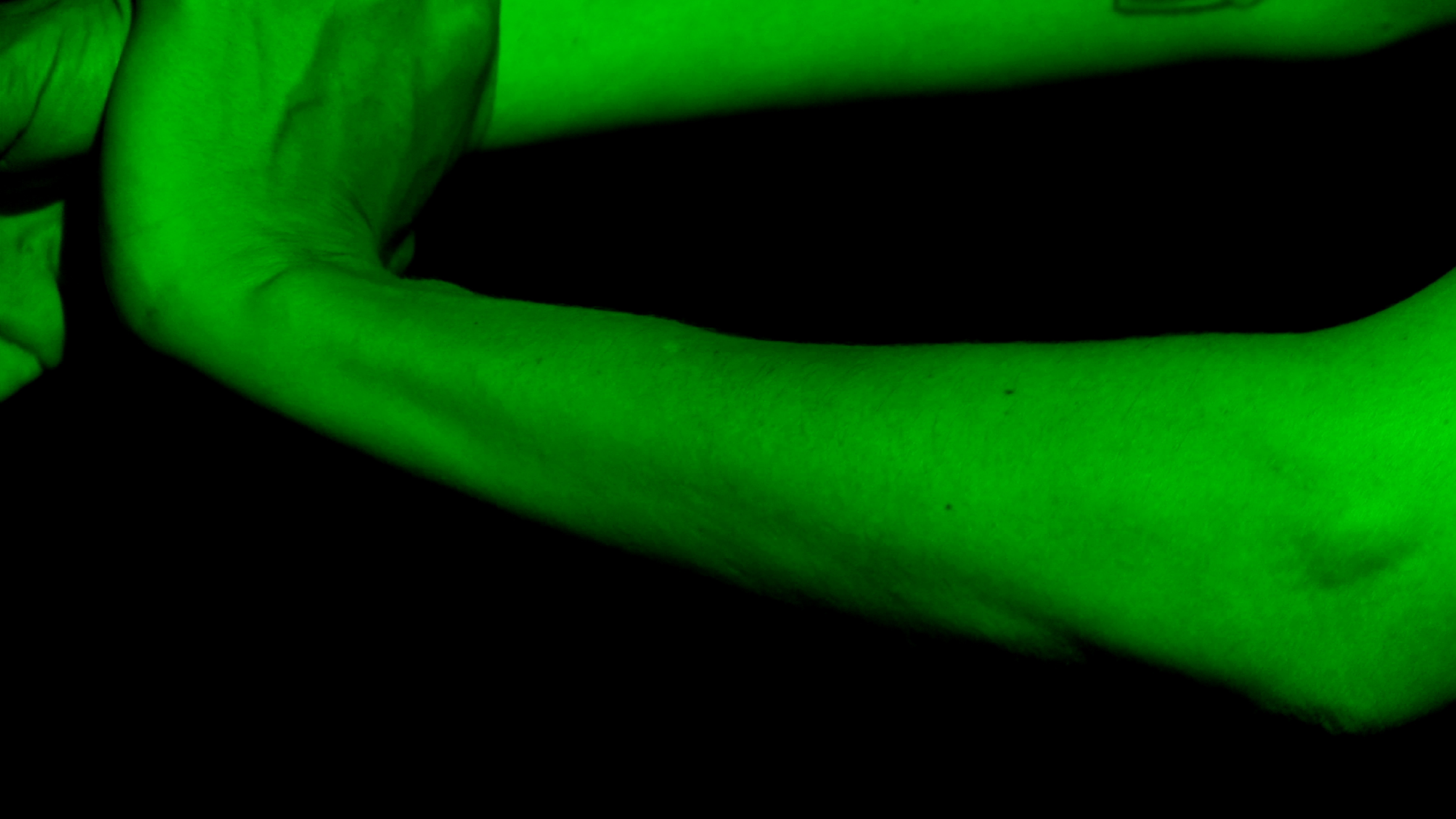 Green colors a close up of arms and hands against a black background.