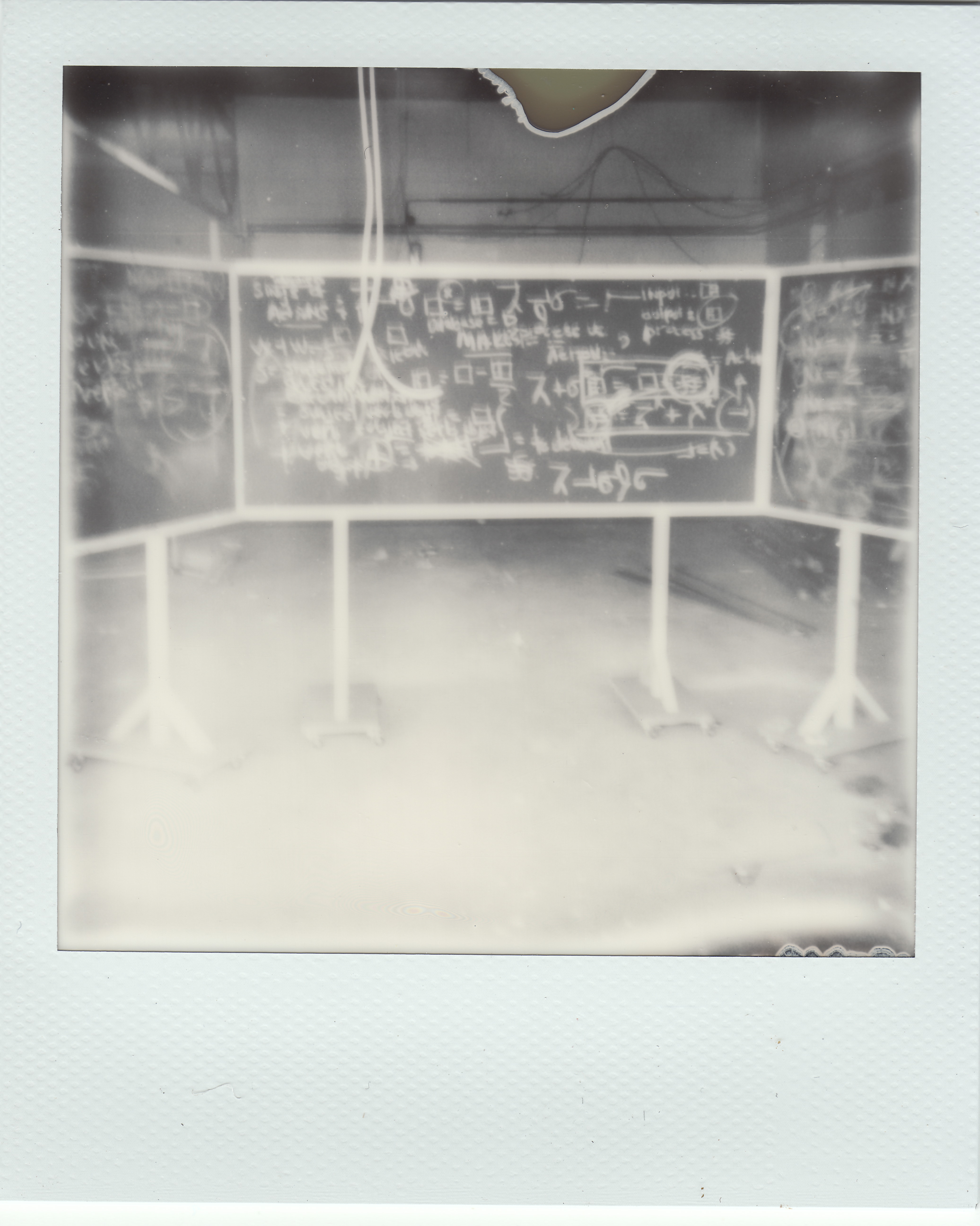 Fogged image of 3 black chalkboards, covered with symbols written in white chalk, in the middle of a dilapidated room