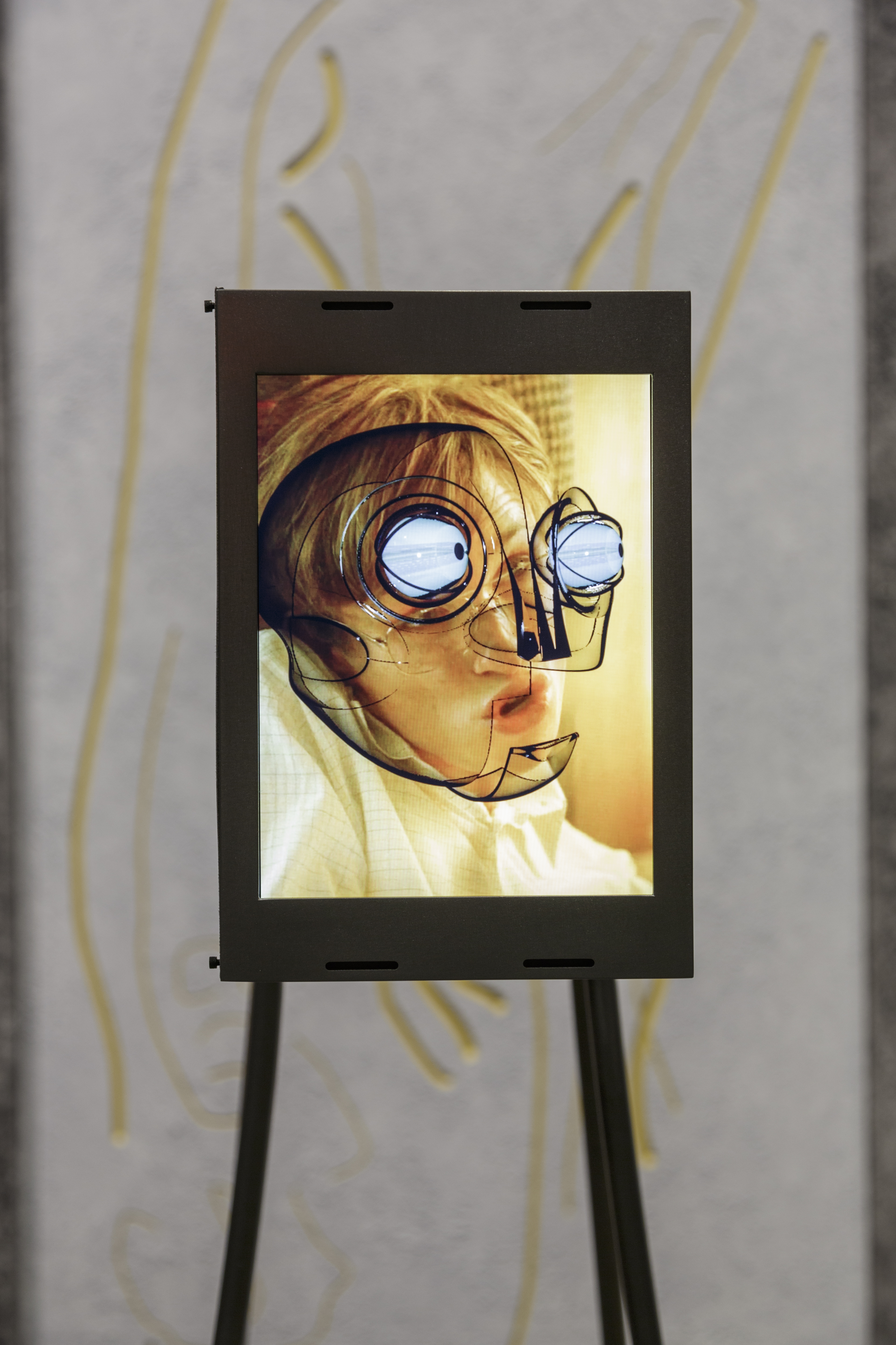 Steel-encased screen shows rendering of robotic face with blue-tinged eye bulbs superimposed on a distorted human face.