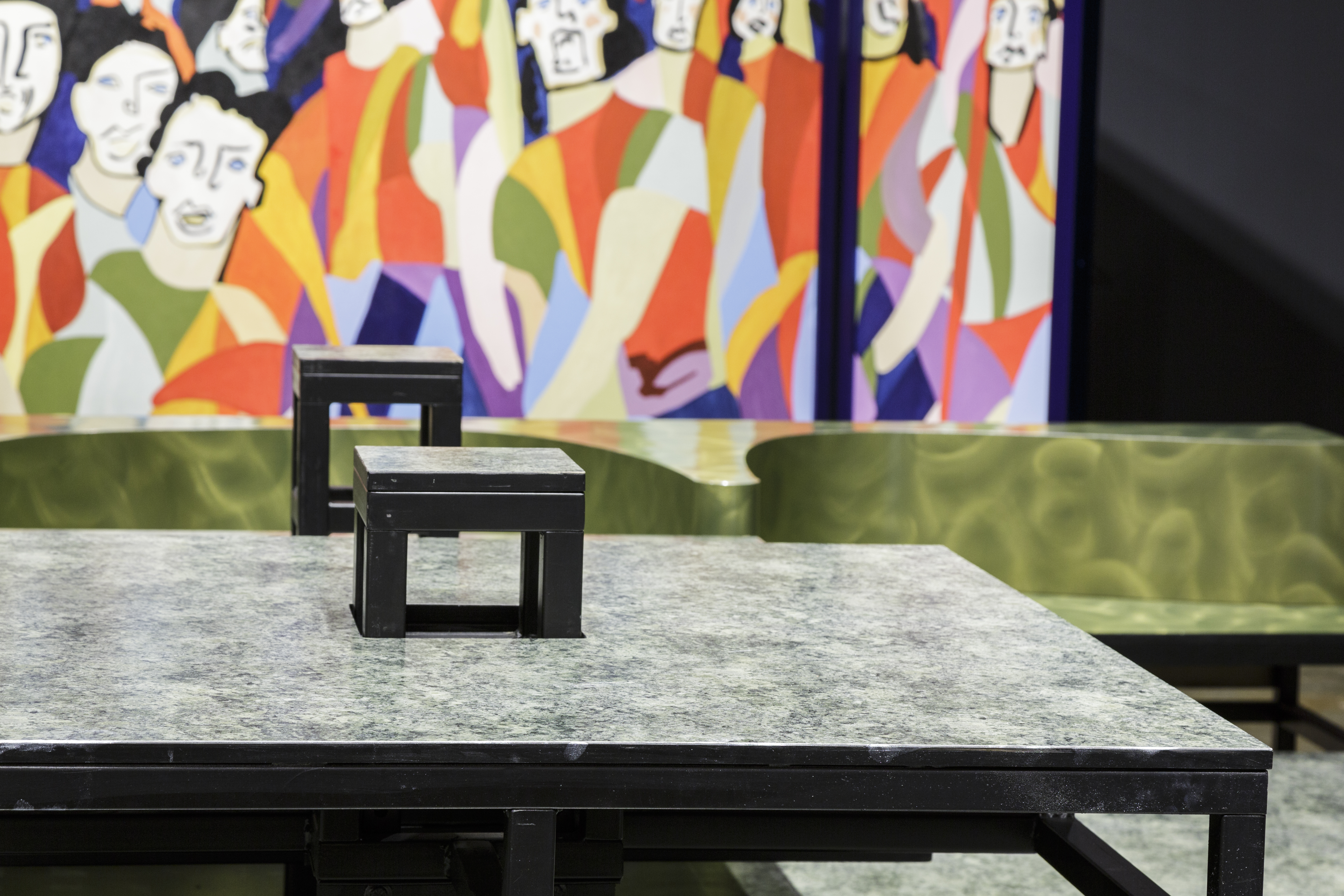 Close-up of a built-in table on stage with a portion of green banquette and trifold screen blurred in the background