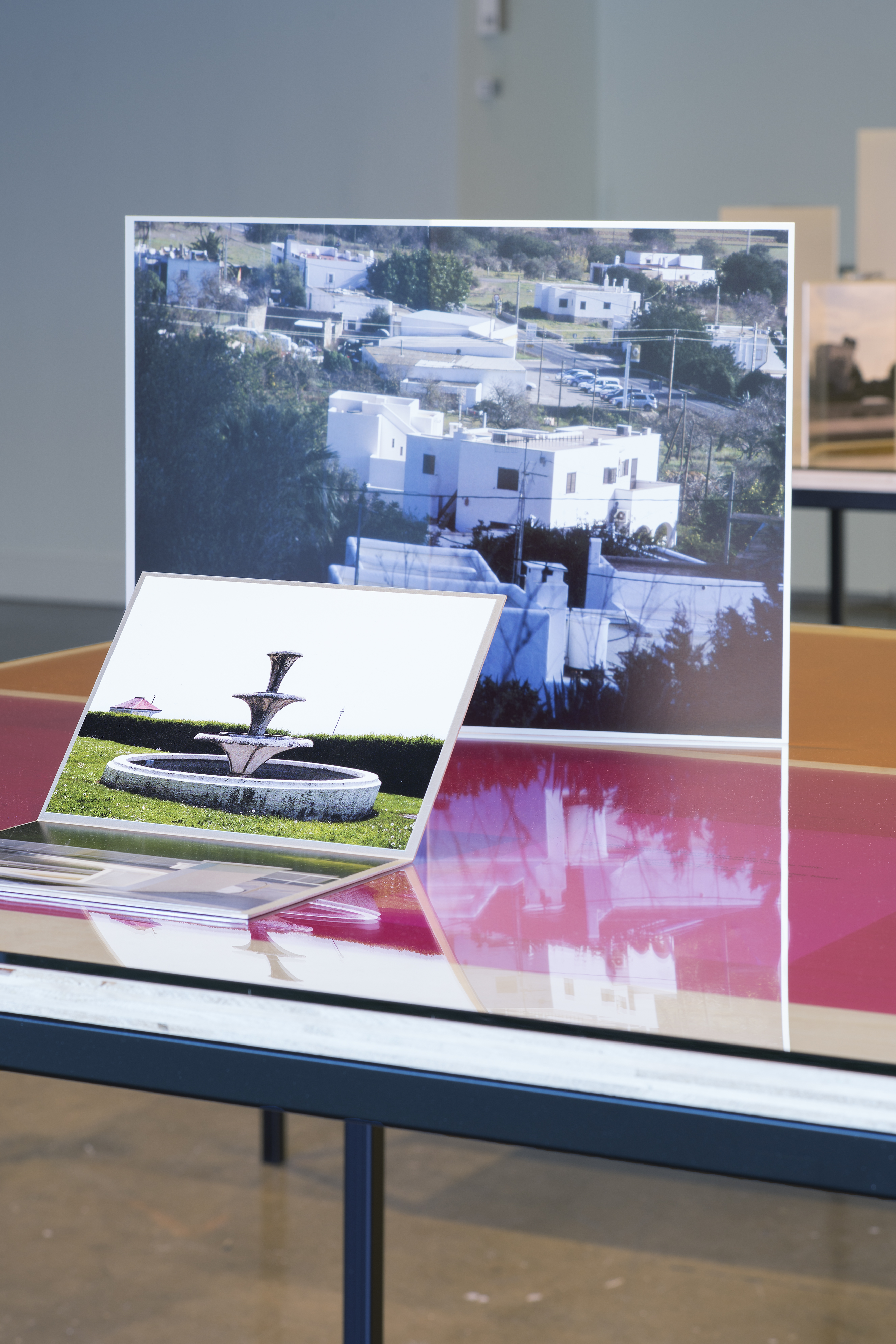 Detail of table top with red and orange gels under glass. Two prints, one of white structures, the other a 3 tier fountain