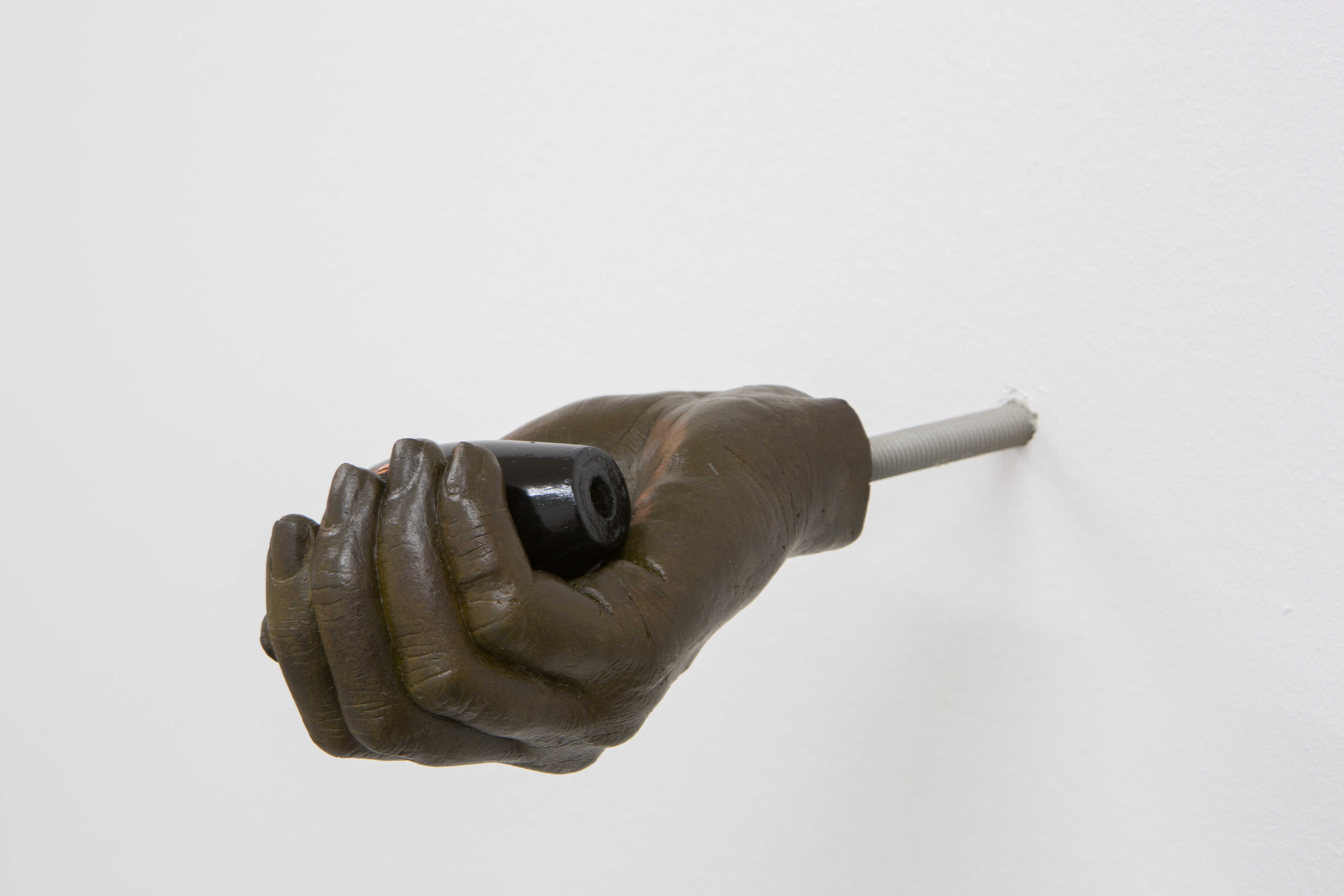 A dark bronze hand emerging from the wall, holding a glass lens with outstretched fingers