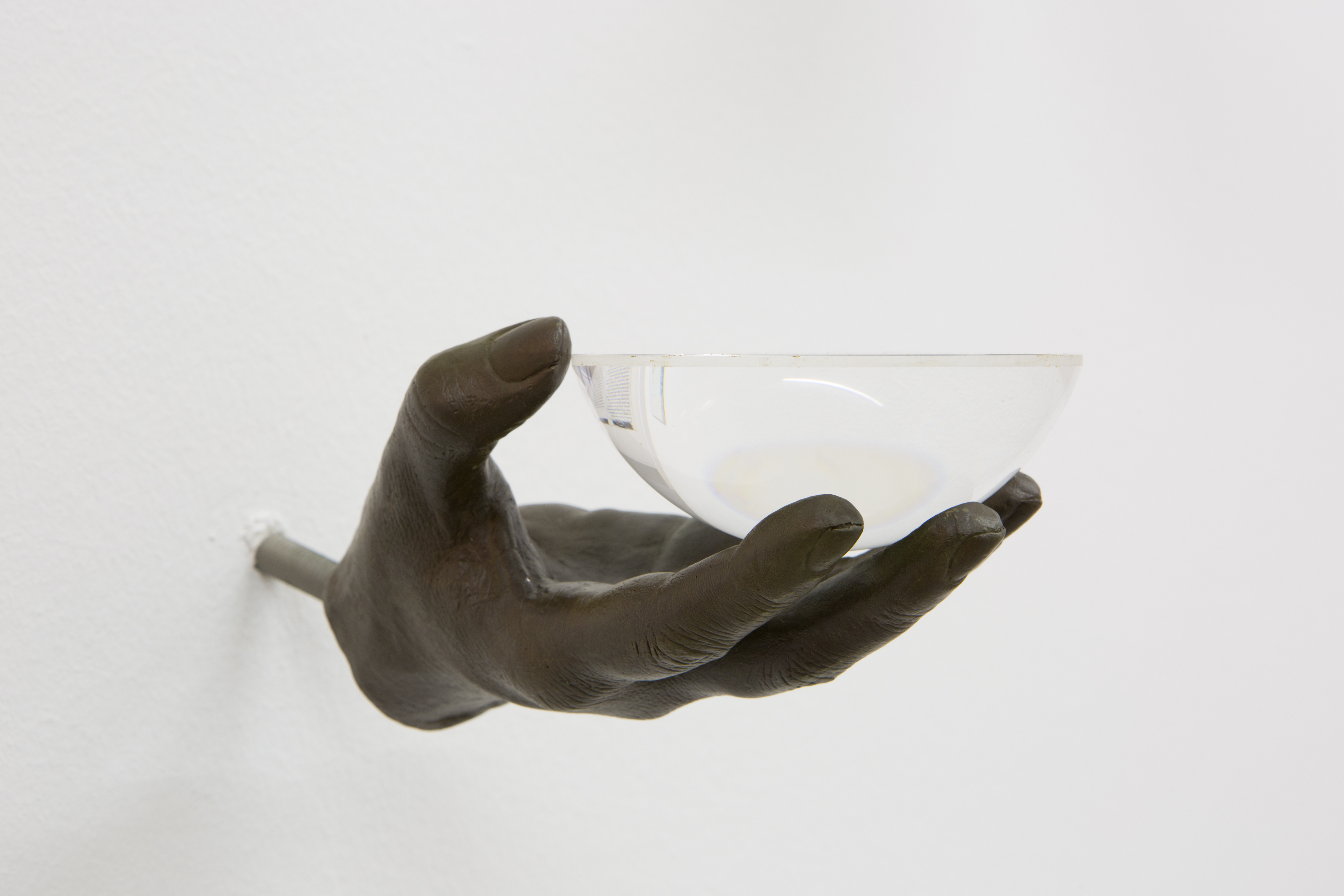 A dark bronze hand attached to the wall by a post, holding a door knob in its upturned palm