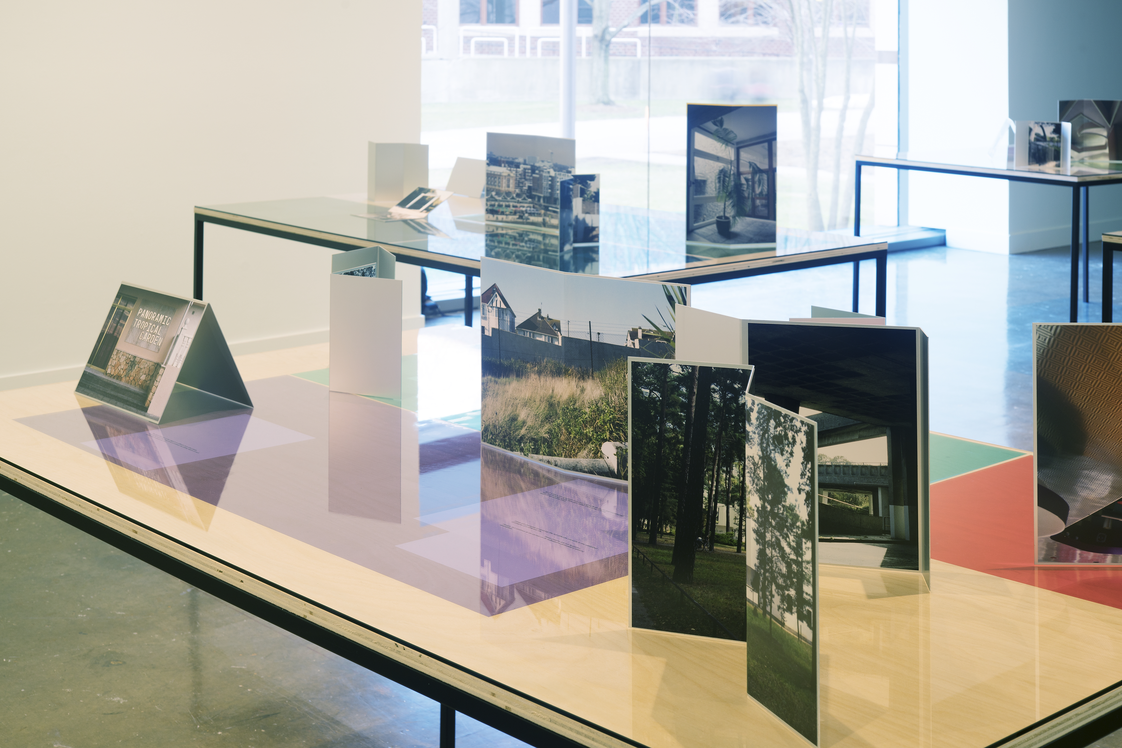 Installation view of table tops with photographs and color gels in front of a picture window letting light in from outside