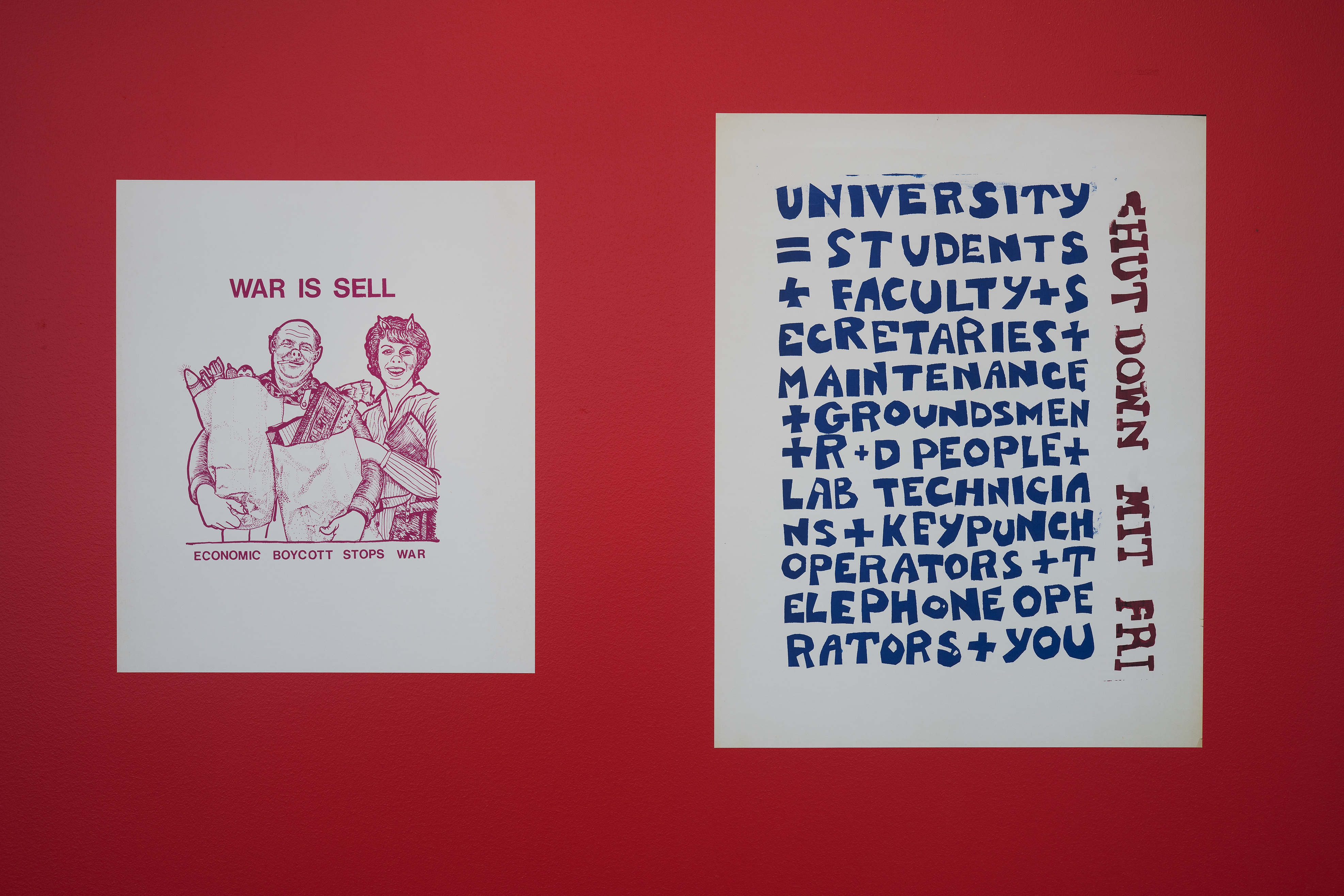 Two graphic protest posters, one supporting economic boycott, the other supporting a walkout, hang side by side on a red wall.