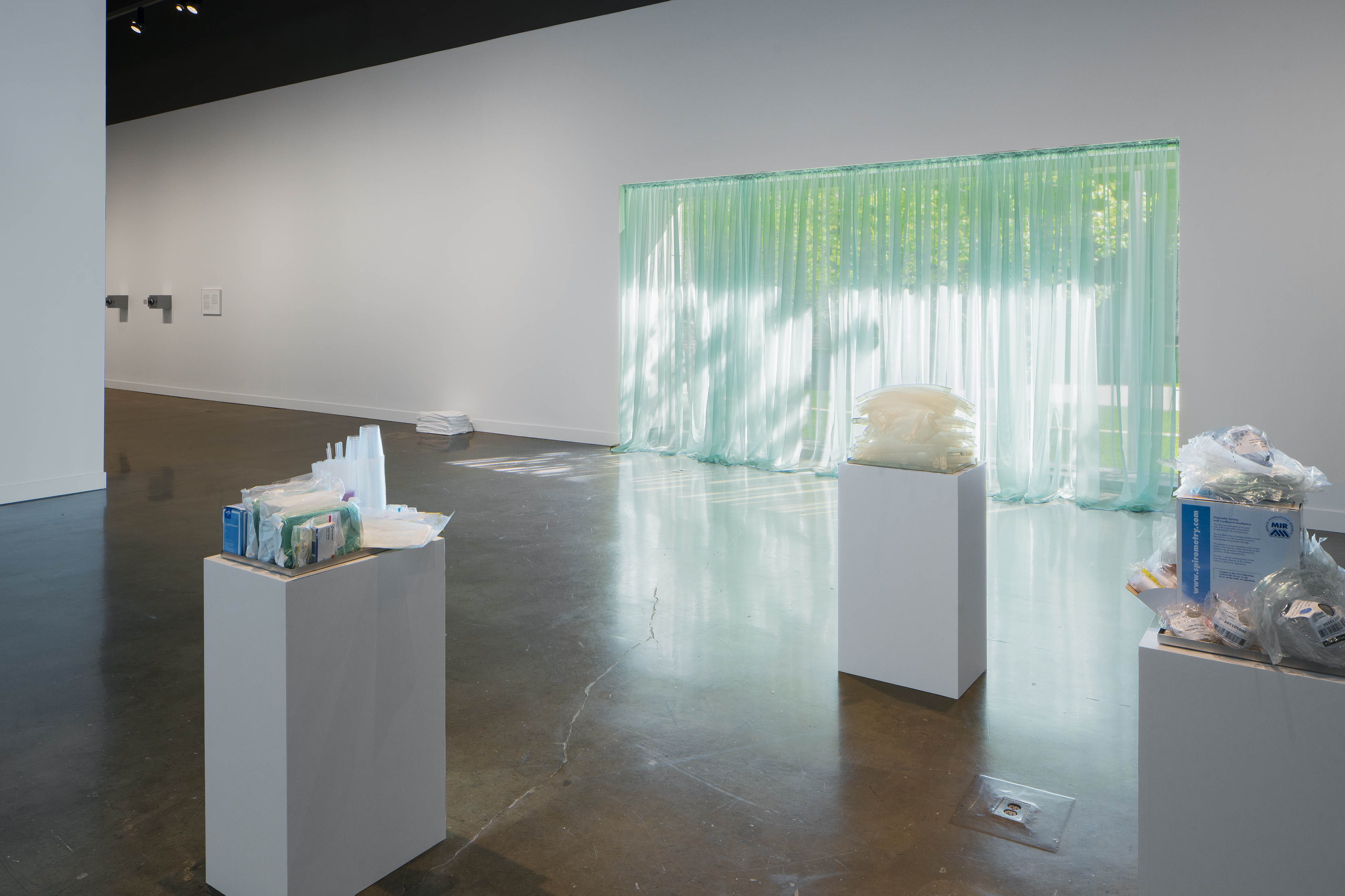 A gallery space has green fabric over the window and art on pedestals.