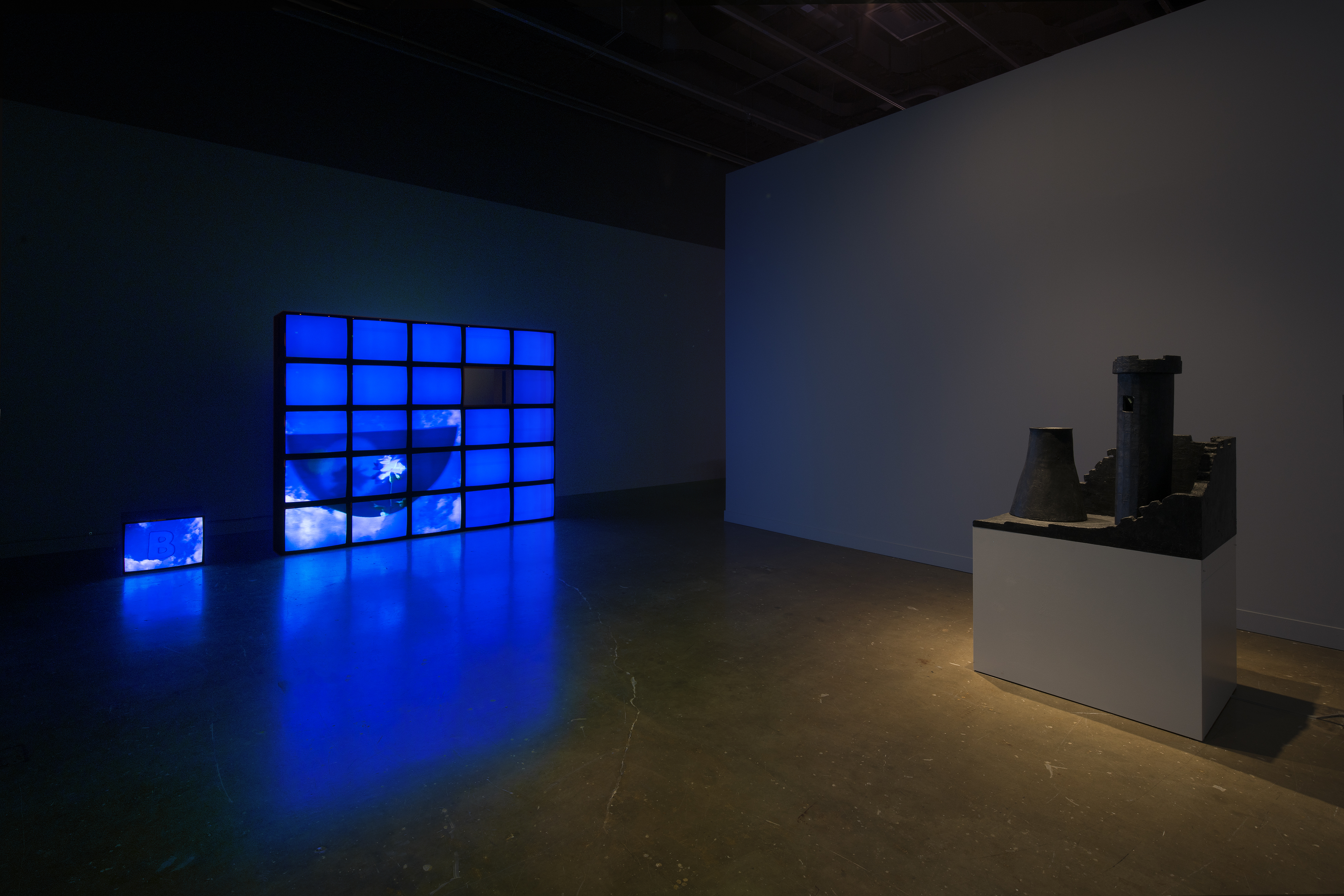 A wall of video monitors display an overall blue image, castle tower with a nuclear stack sits on a pedestal in front.