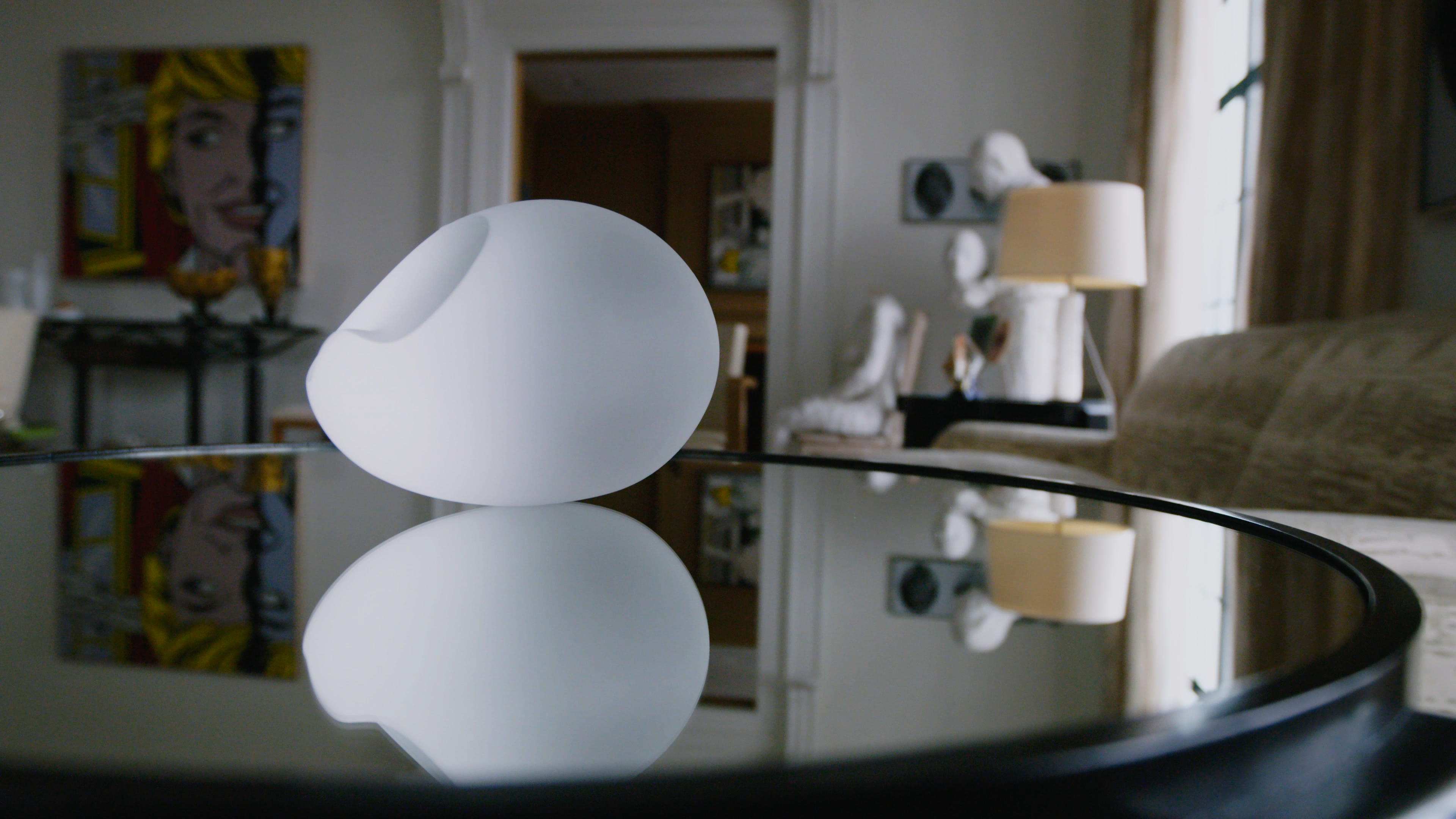 Video still of frosted crystal object on a mirrored table, reflecting its image and surrounding art filled room.