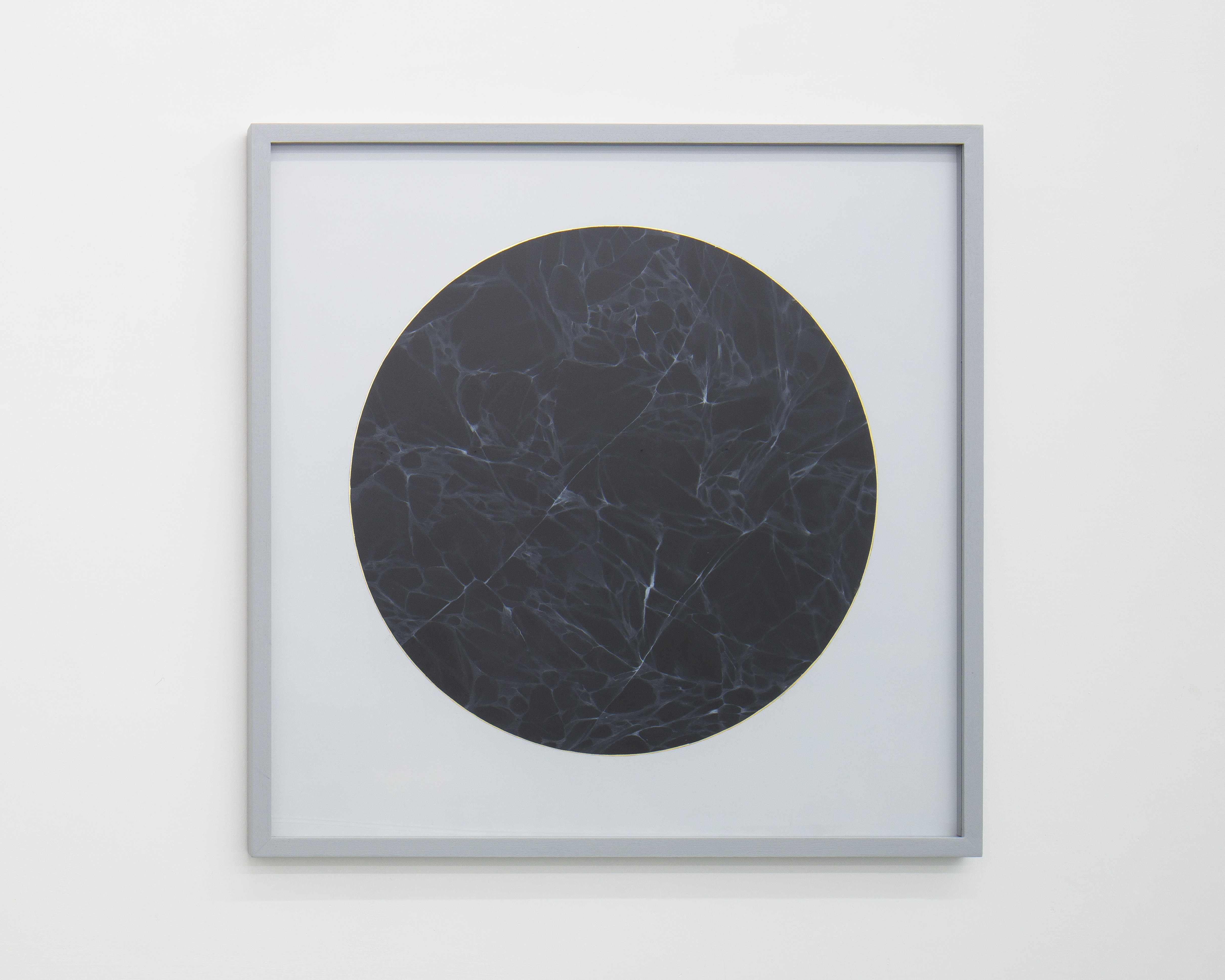Gray square frame surrounds painting of a circle of black veined marble outlined with gold leaf on paper.