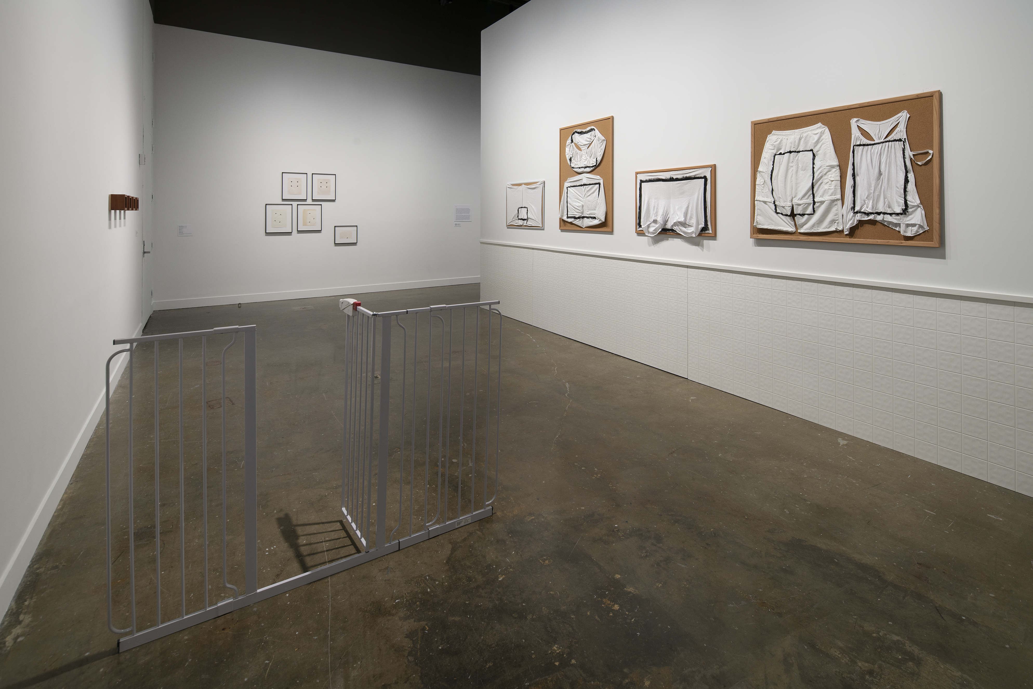 A freestanding gate with an open door, 4 bulletin boards with painted underwear to the right, 5 framed objects to the rear.