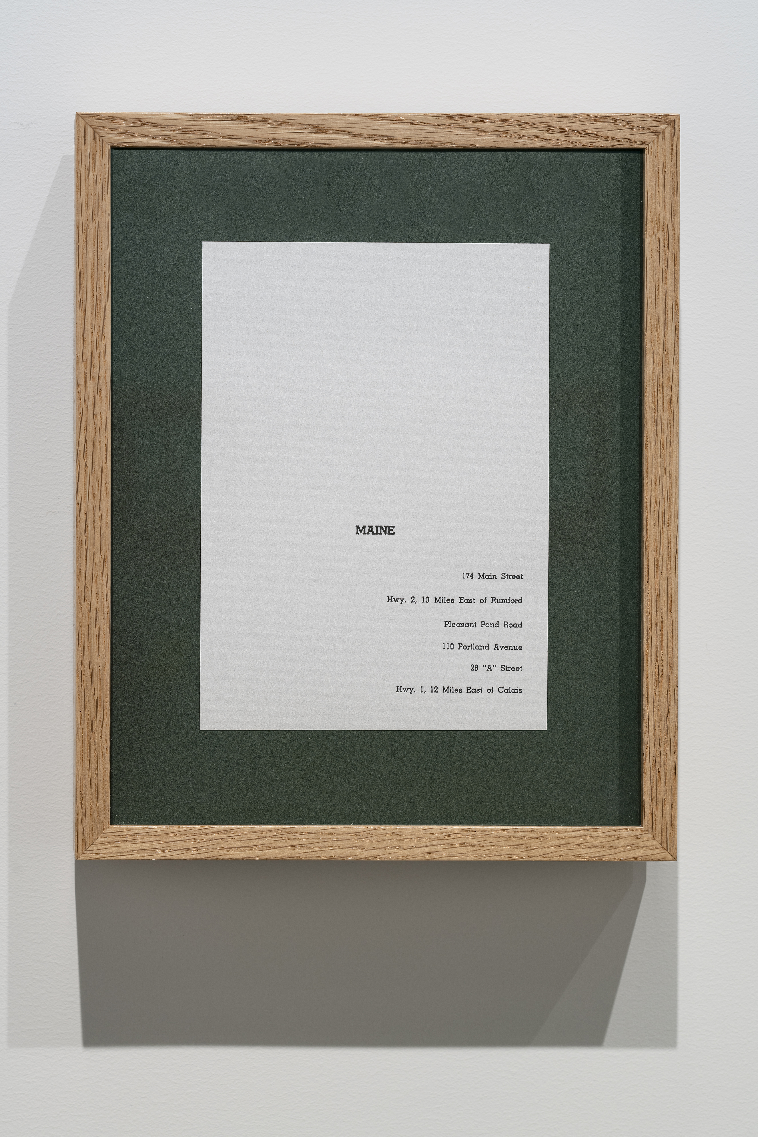 A vertical wooden frame with green matting and a piece of paper on which the name, Maine and 6 partial addresses are typed.