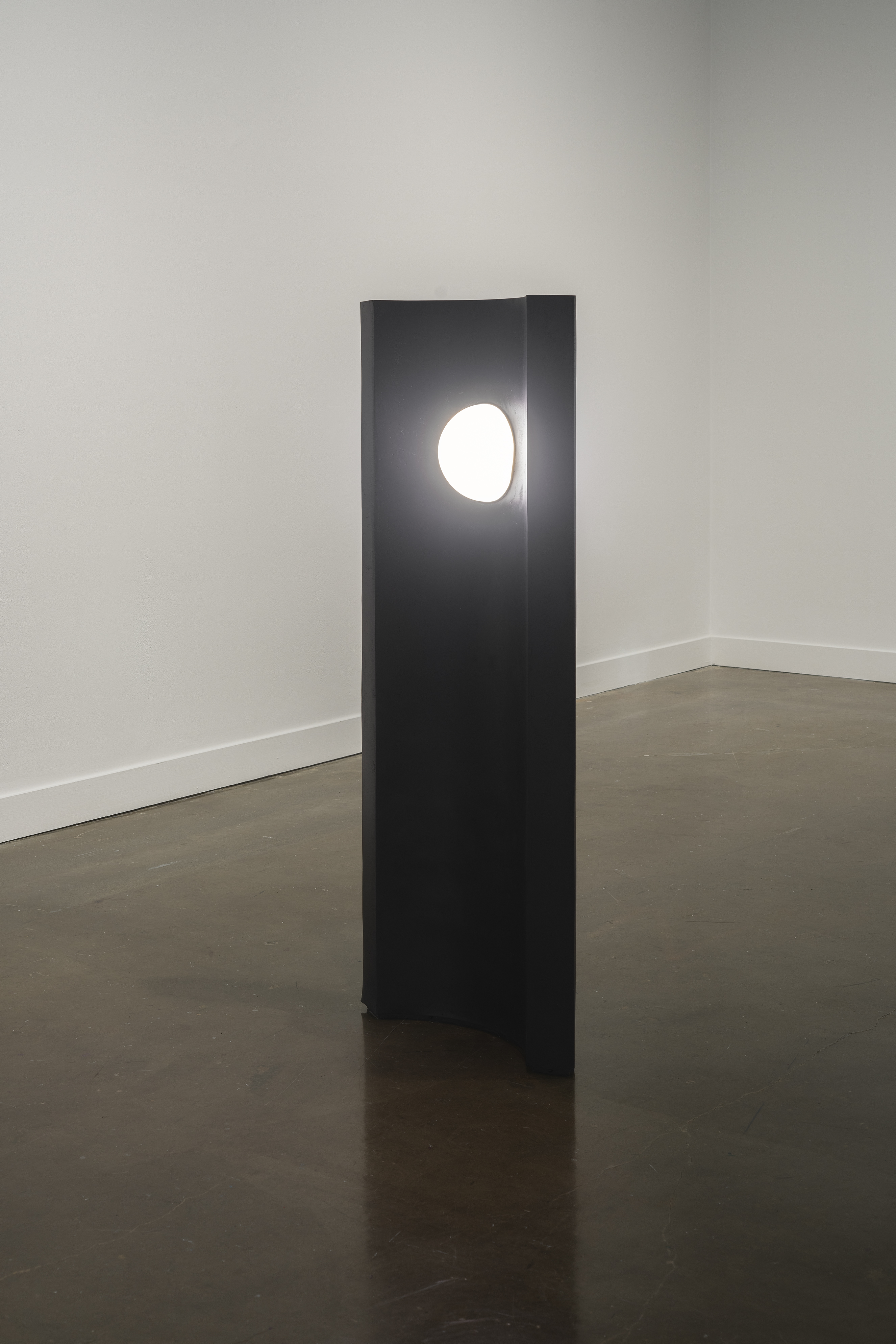A convex, black tower with an orb of light in the center near the top stands alone in the Gallery.