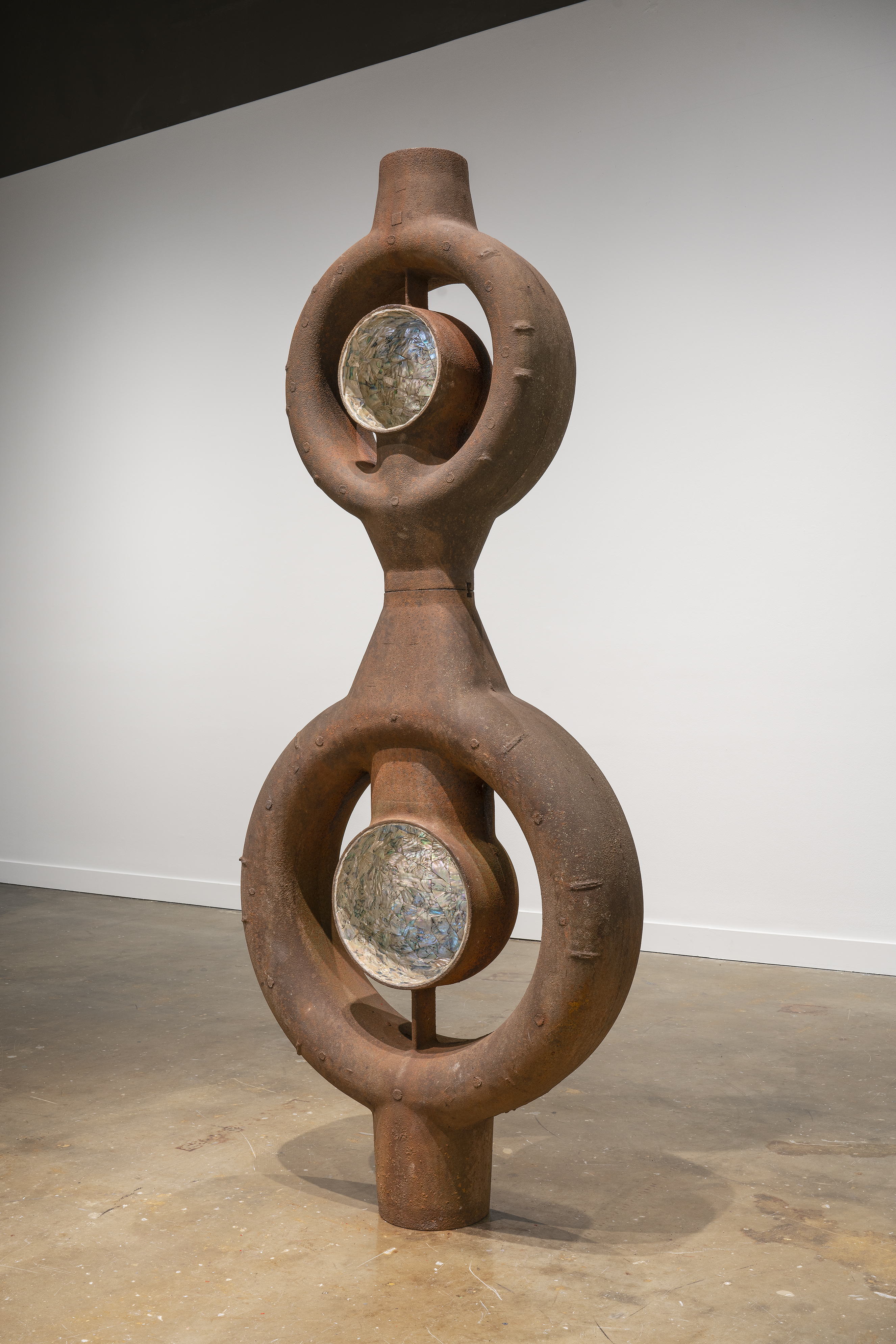 Large, standing, rusty metal object with two open circles in which smaller circles are inlaid with shimmering abalone.