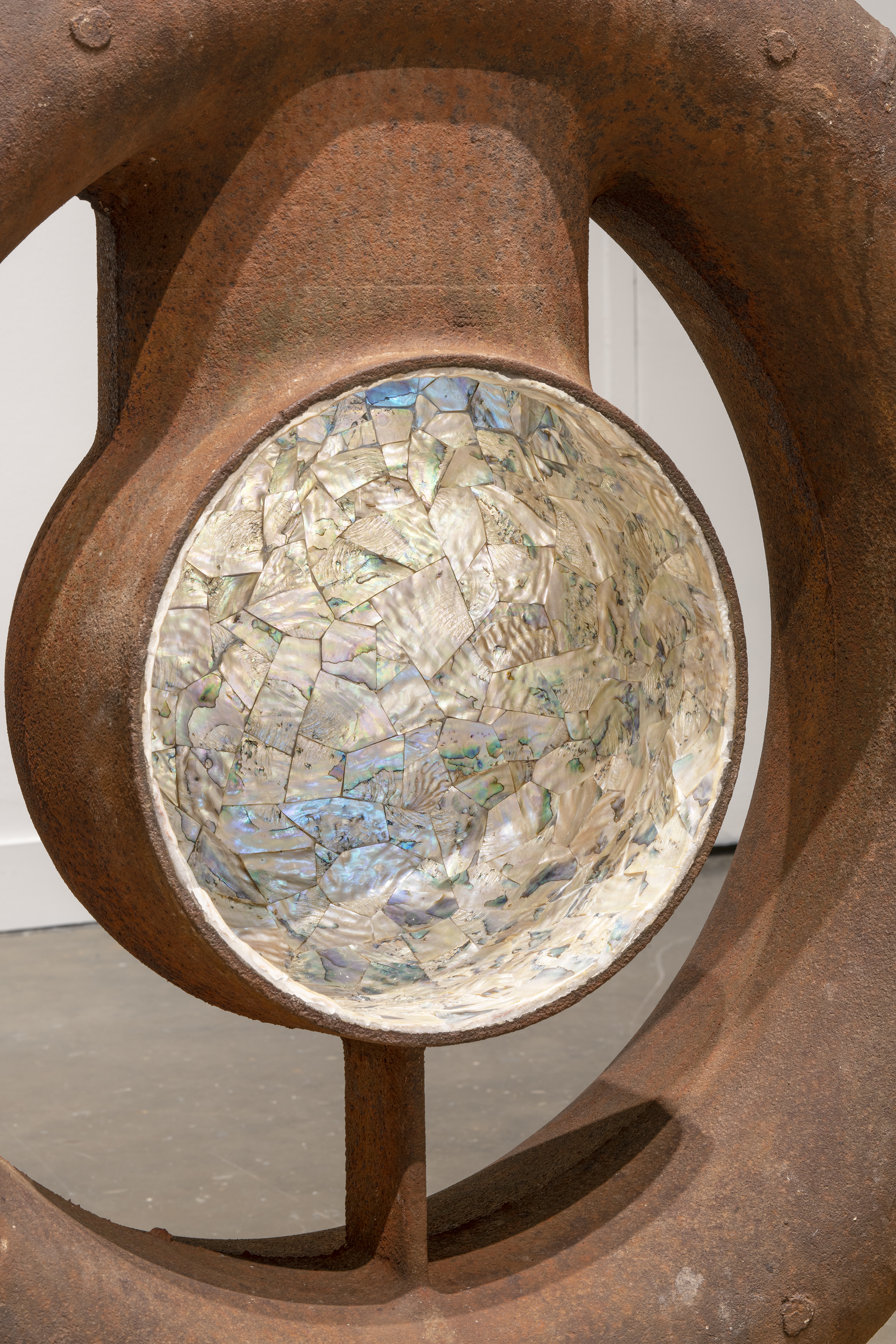 Close view of shimmering abalone mosaic inlaid in a gourd-like portion of a ship’s rusted, pitted, metal boiler.