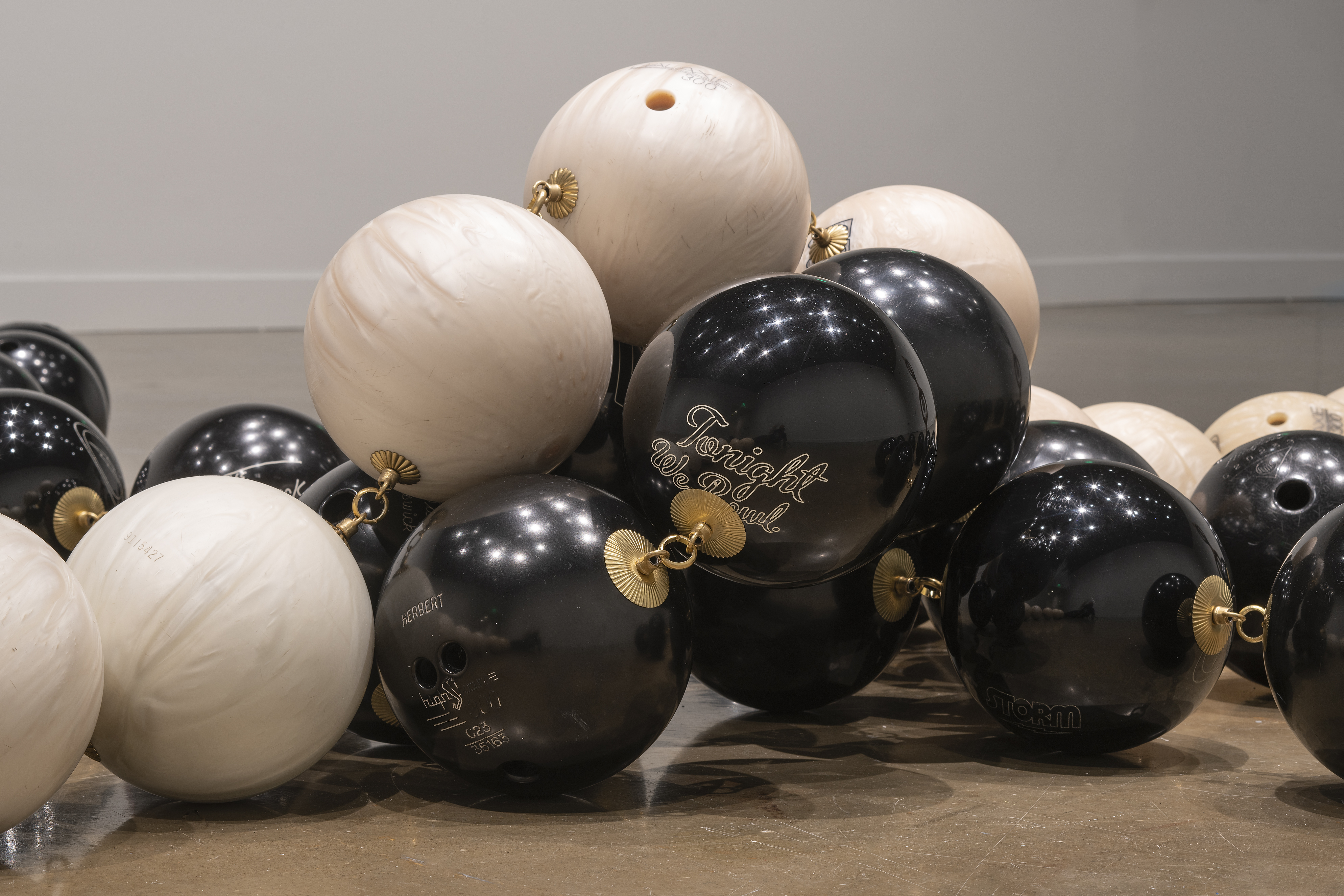 Close view of black and white bowling balls, each linked with brass hardware. Tonight, written in script, is visible on one ball.