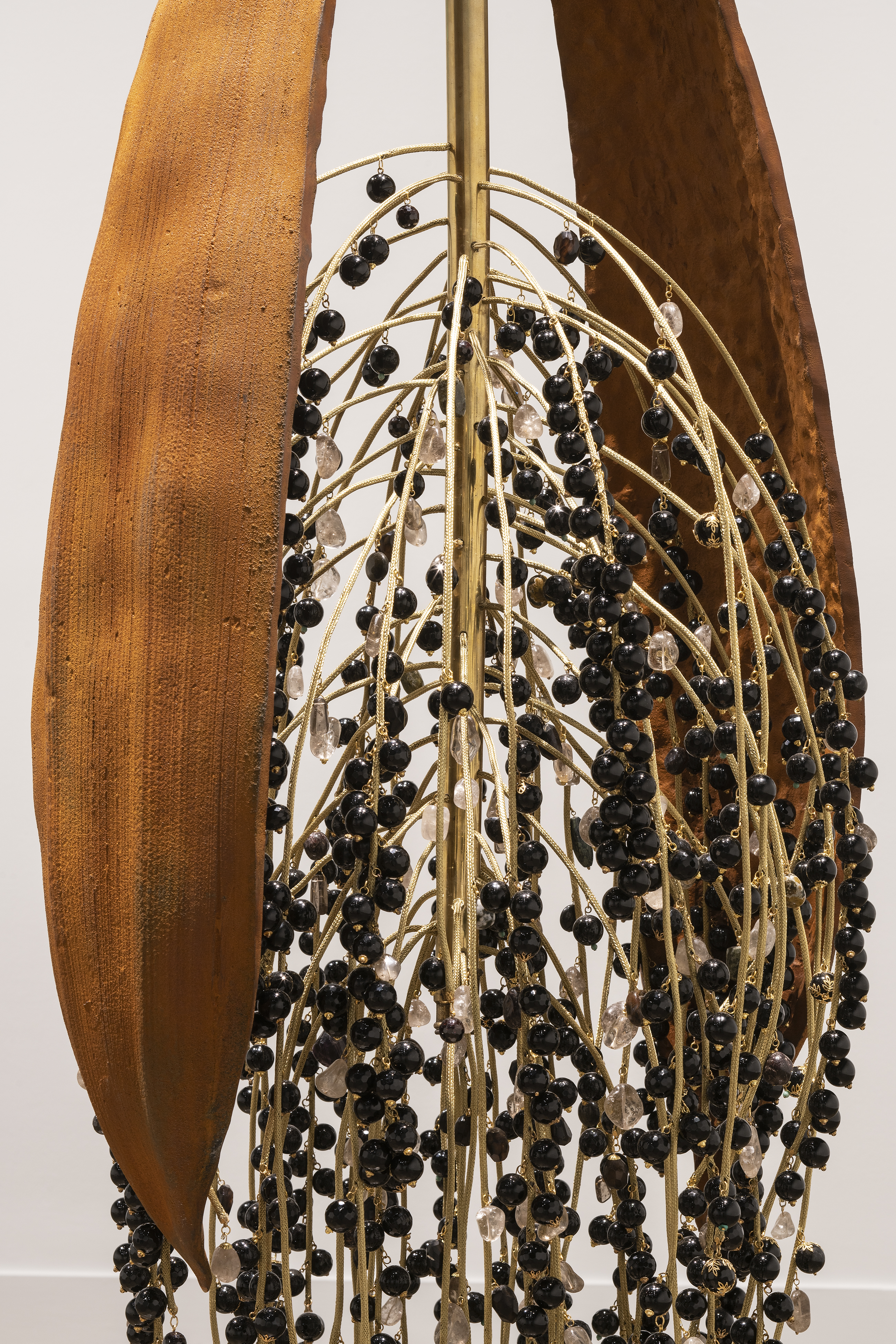 Close view of rust-colored, textured metal frond on the outside of onyx beads cascading down on gold metal stems.
