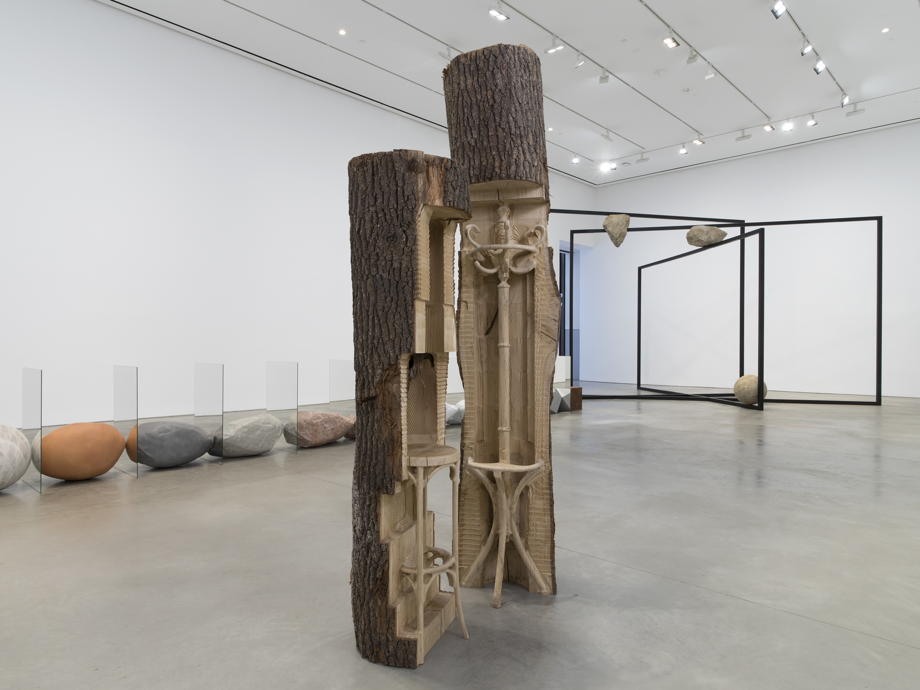 Two wooden logs with carvings are featured in a gallery space.