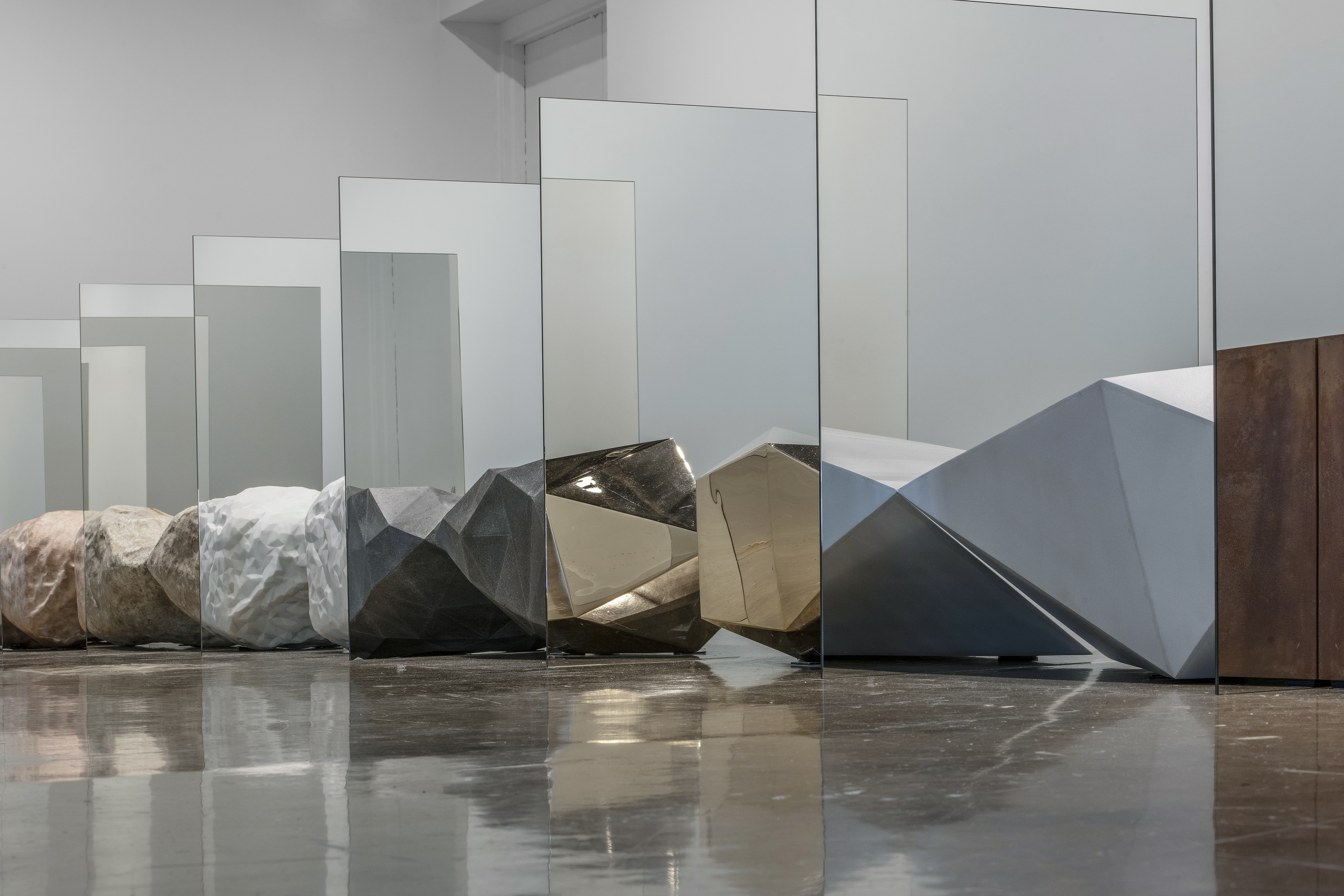 Detail view of objects resembling precious rocks are arraged in a straight row. Between each object is a mirror, creating the illusion that each rock is morphing into one another.