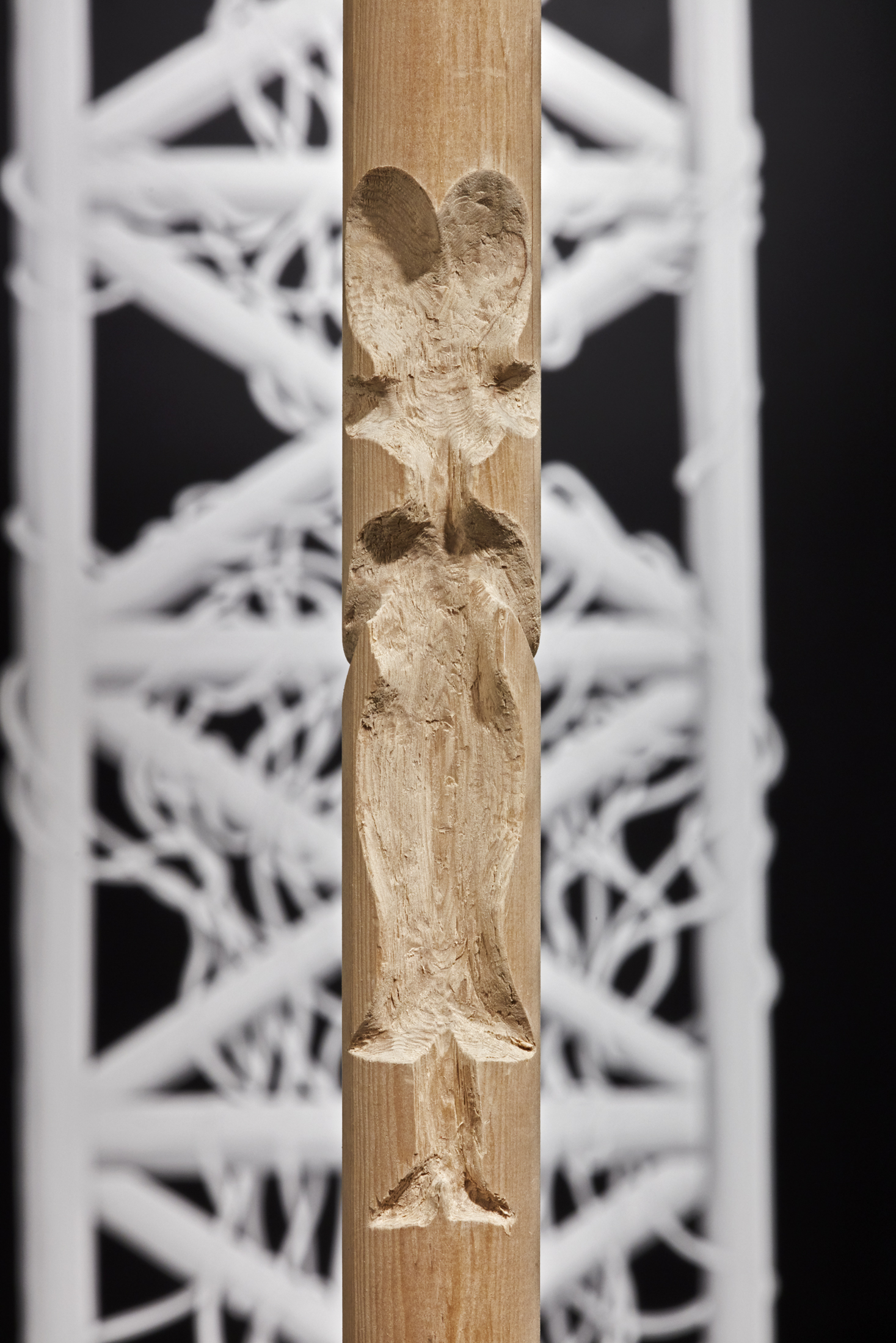 Detail view of woodel pole at center of gallery with the small cutout shape of a female figure with large hair.