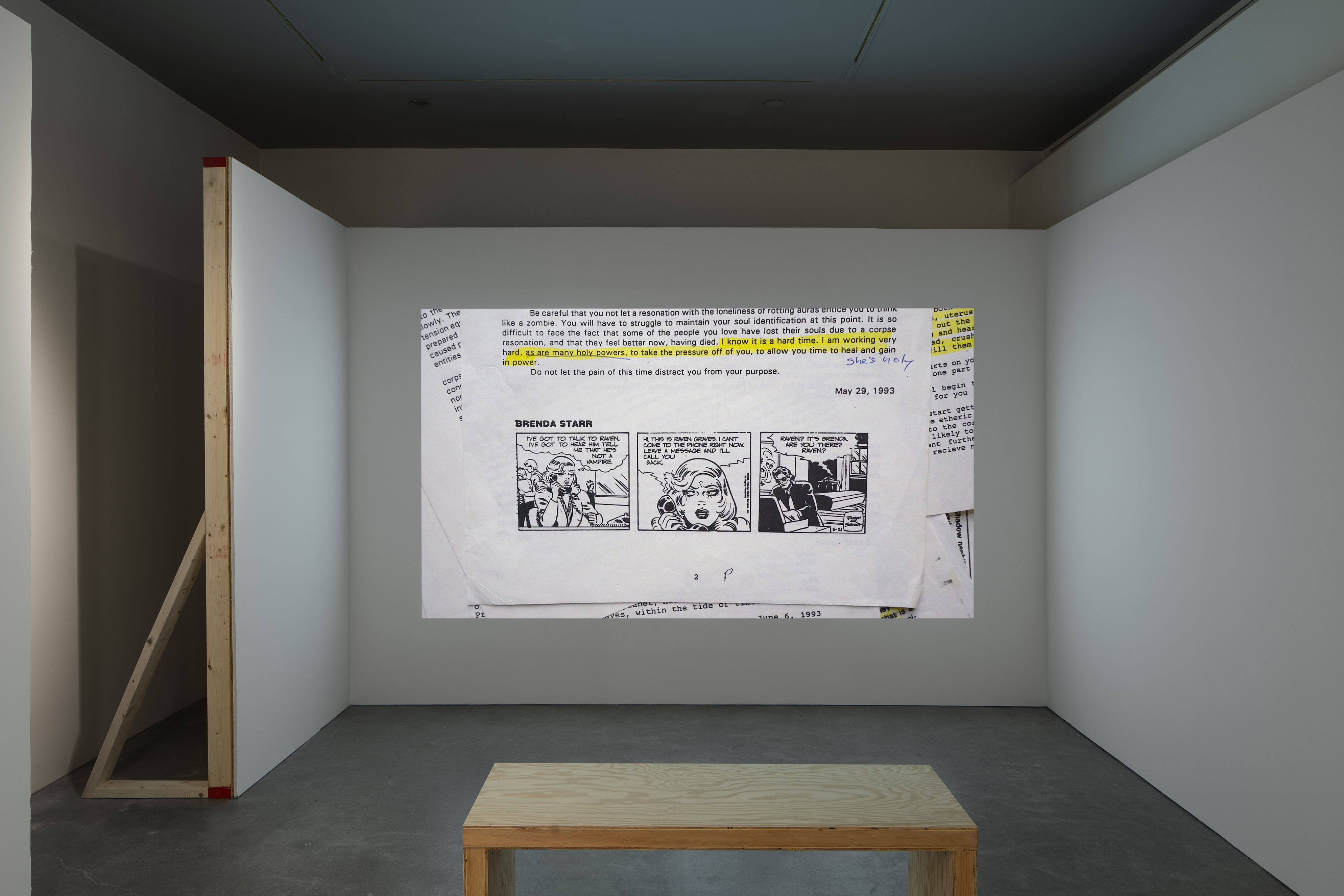 Still of papers, on top, a partial page with yellow-highlighted text above a black and white, 3-frame “Brenda Starr” cartoon