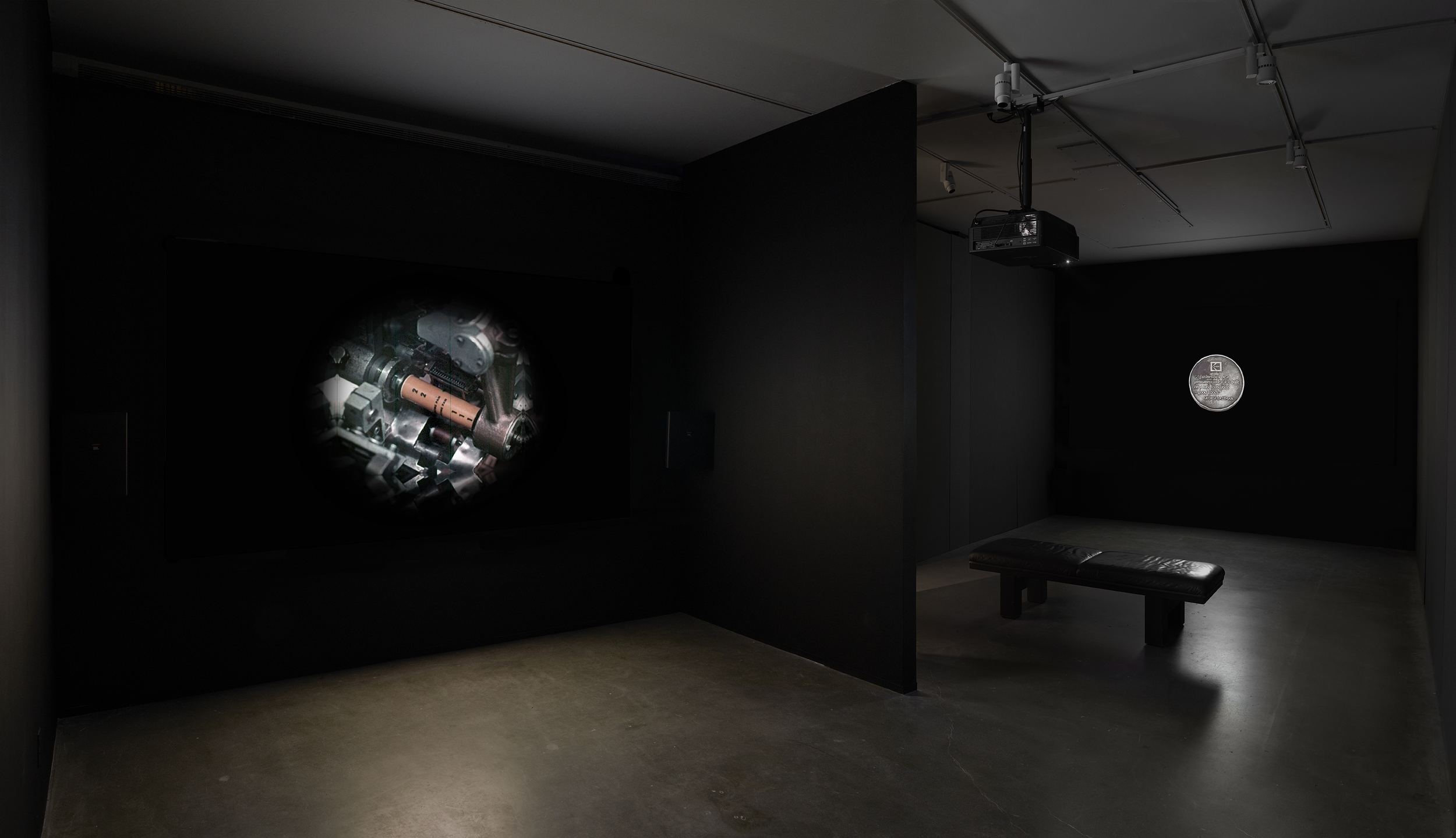 A dimly lit gallery space includes a screening of a storm tropper with its back turned to the screen and a soft bench.