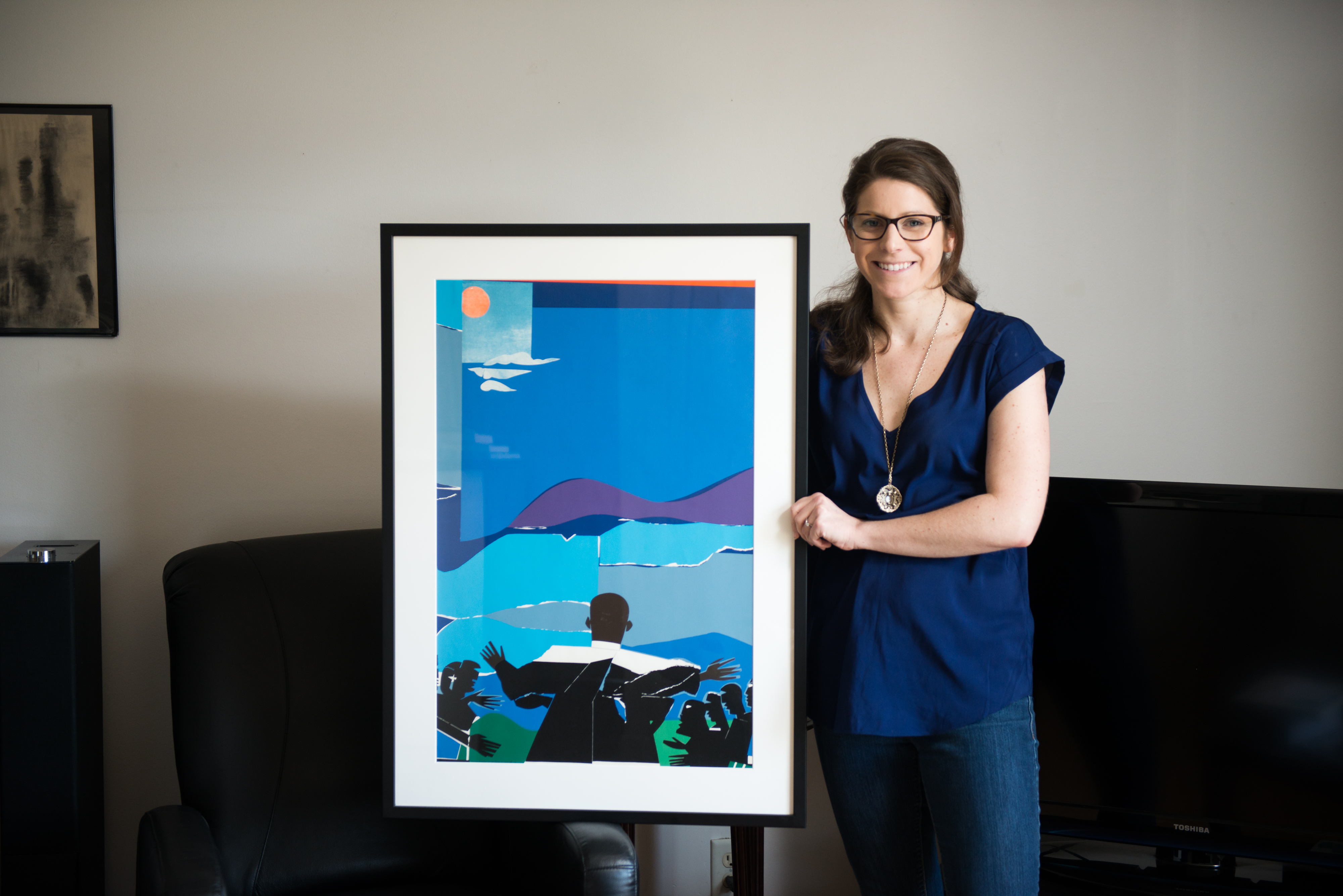 A woman in a blue shirt poses with a painting.