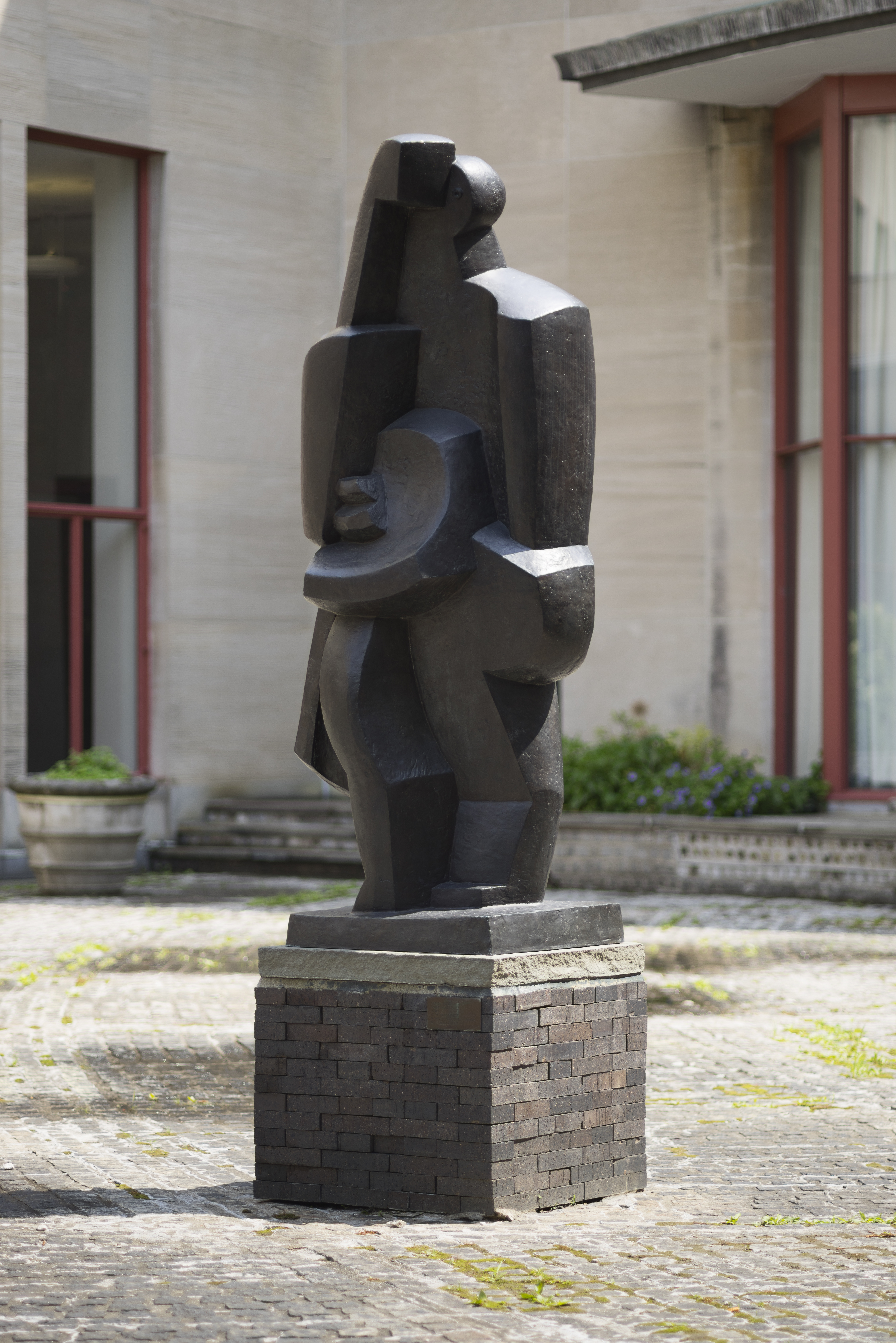 Bronze sculpturea nude figure standing in a relaxed pose with fabric draped behind their back in a stone courtyard.