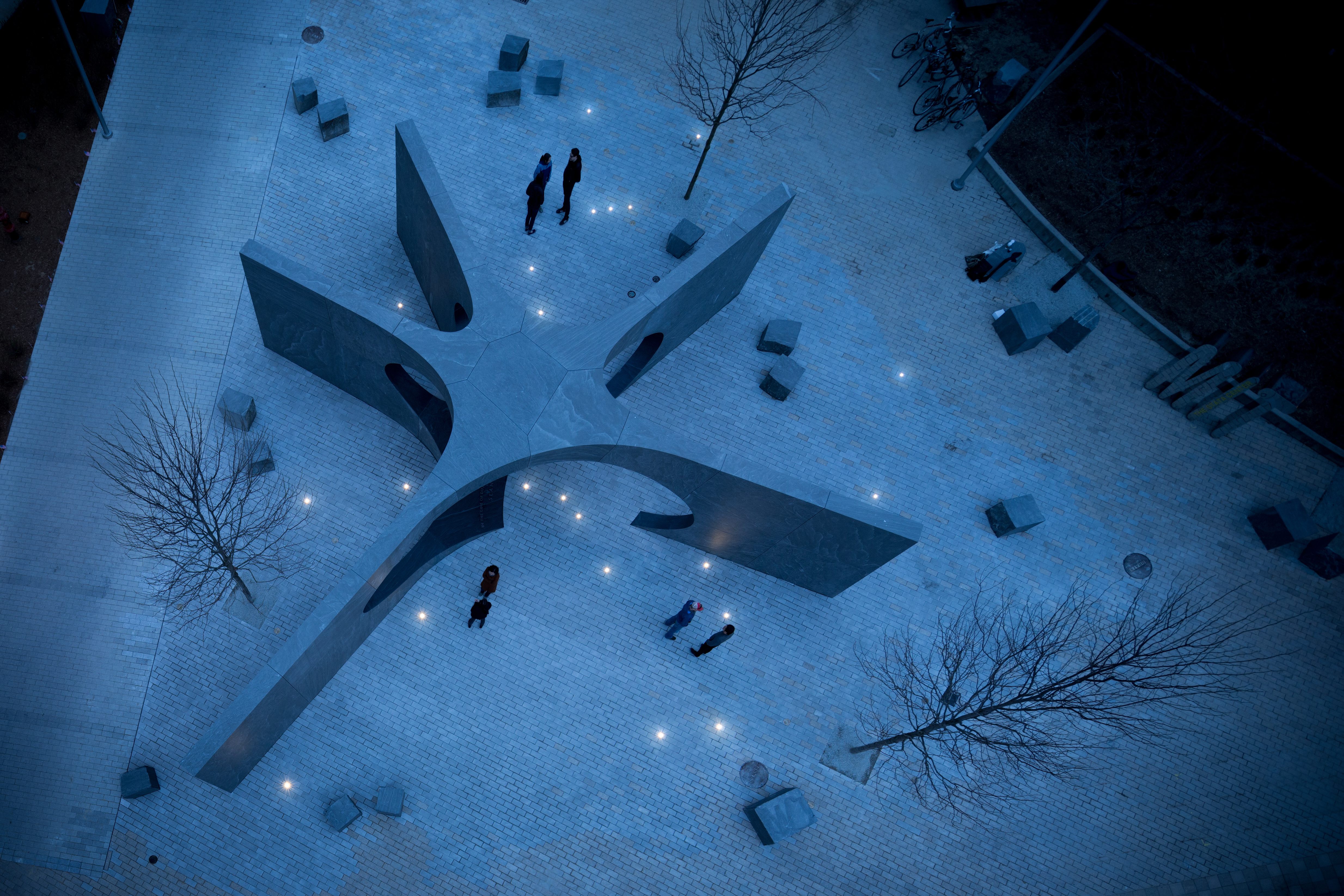 Overhead view of a memorial featuring blocks of granite that support each other to form an empty spacethat extends outward in five directions