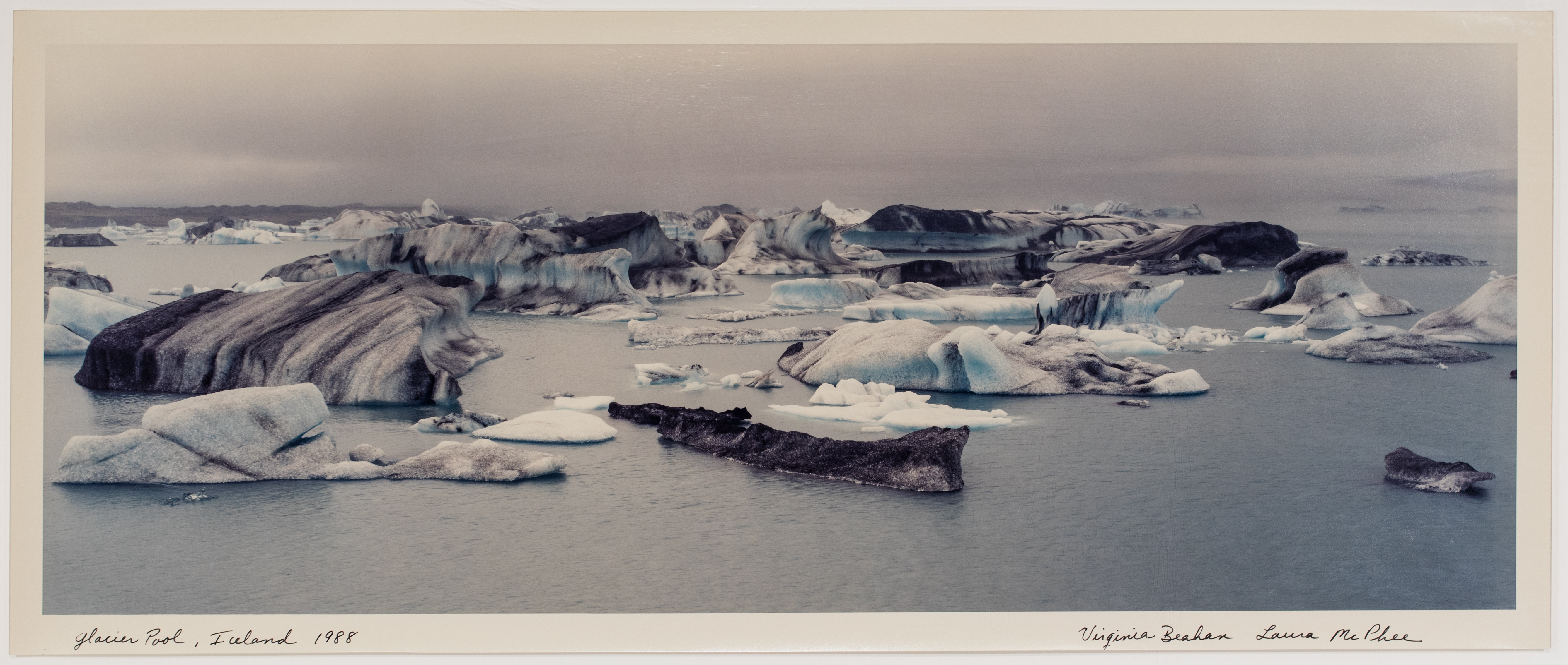 Photograph of glaciers on a still ocean with a cloudy sky behind.