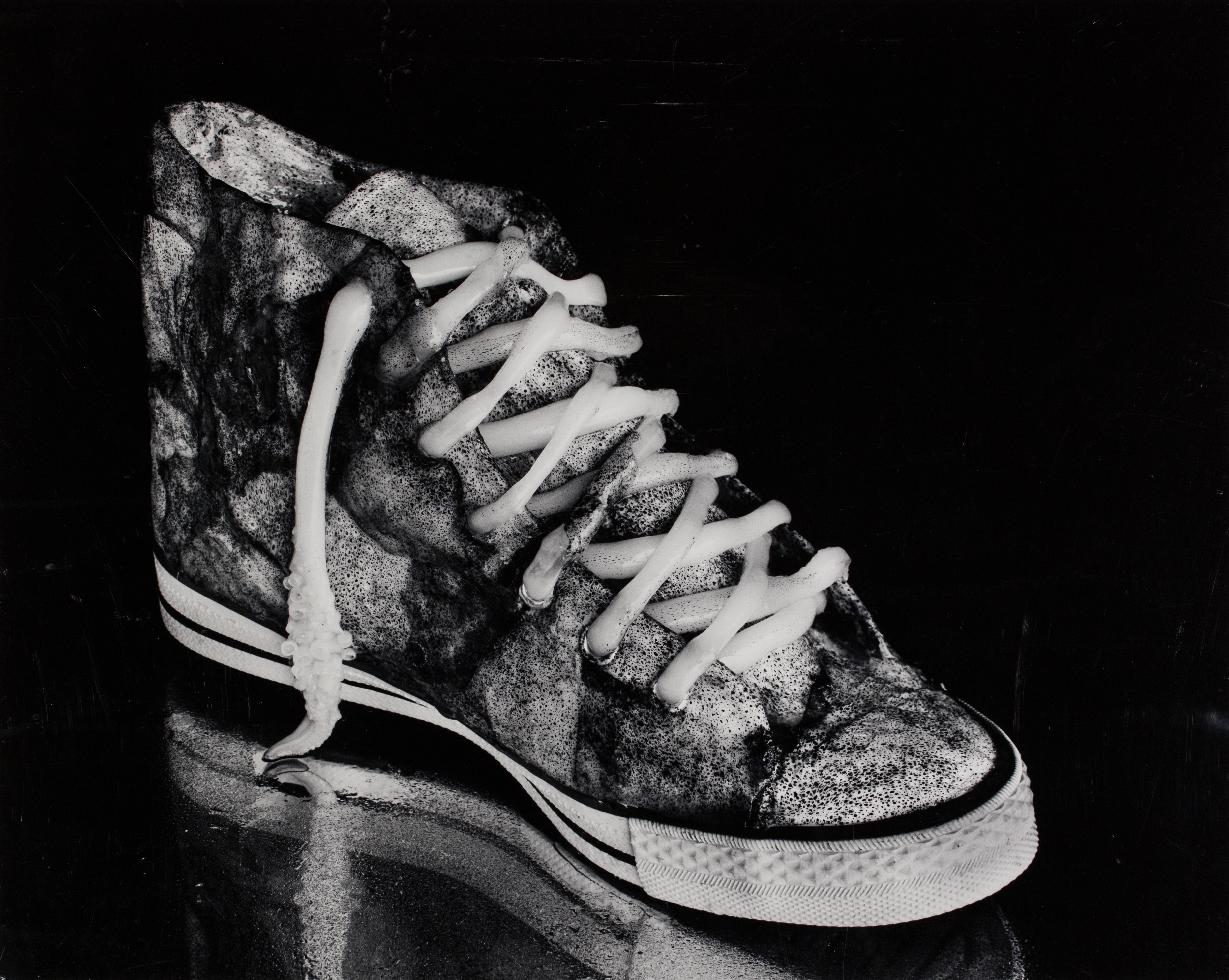 A dirty high top sneaker with a slight reflection below it and a black background.