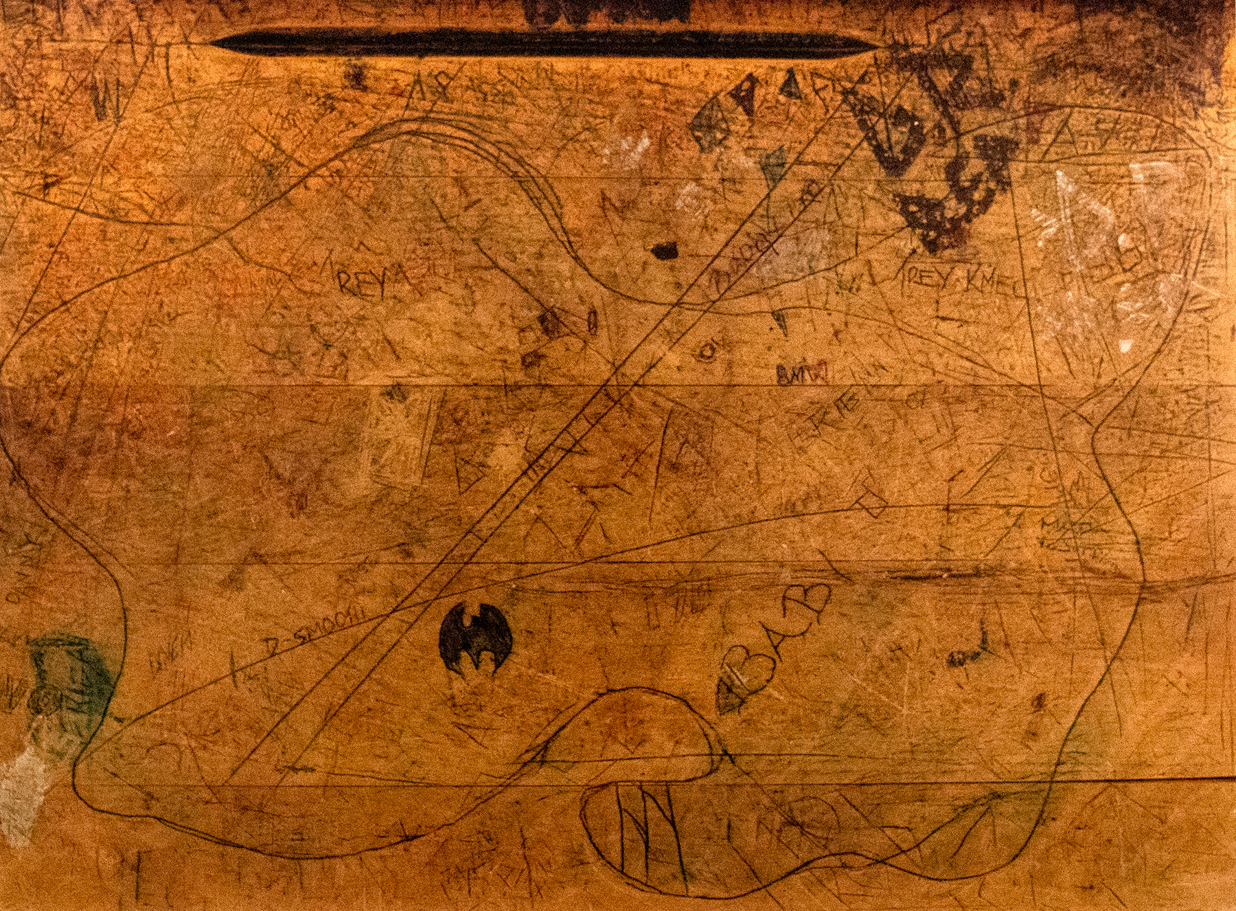 Photograph of the surface of a desk with lots of scribbles and lines written and carved into it.
