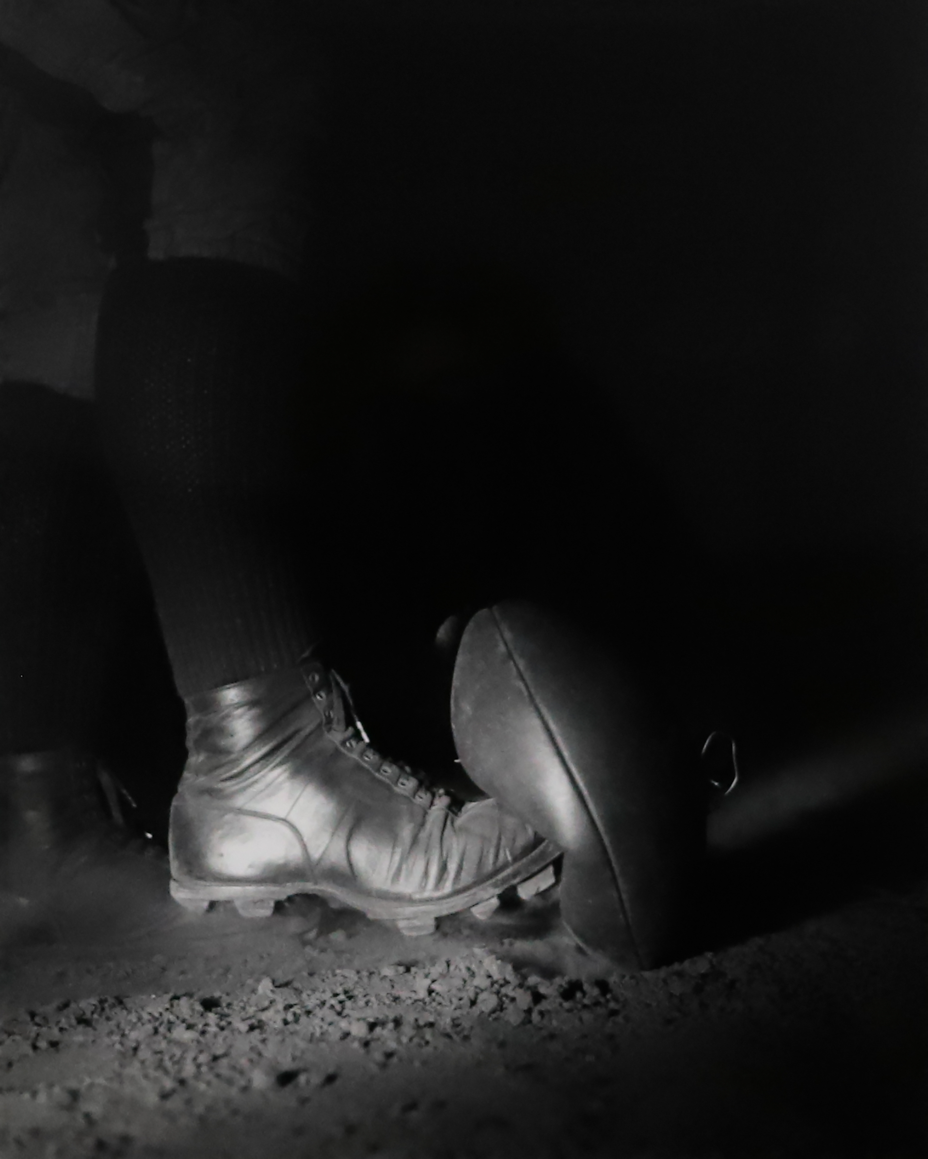 Black and white photograph of a cleat pressed up against a football ready to kick it.