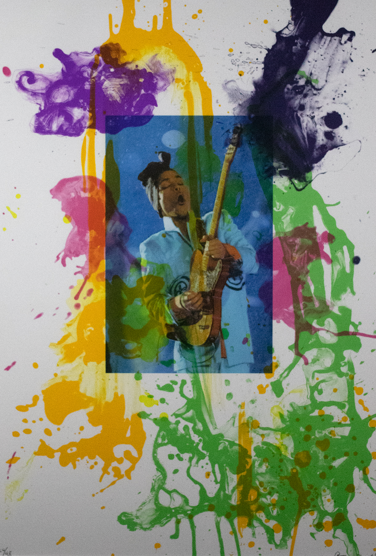 Photograph of a woman playing the guitar placed in the center of a canvas with green, purple, yellow, and pink ink splattered around it.