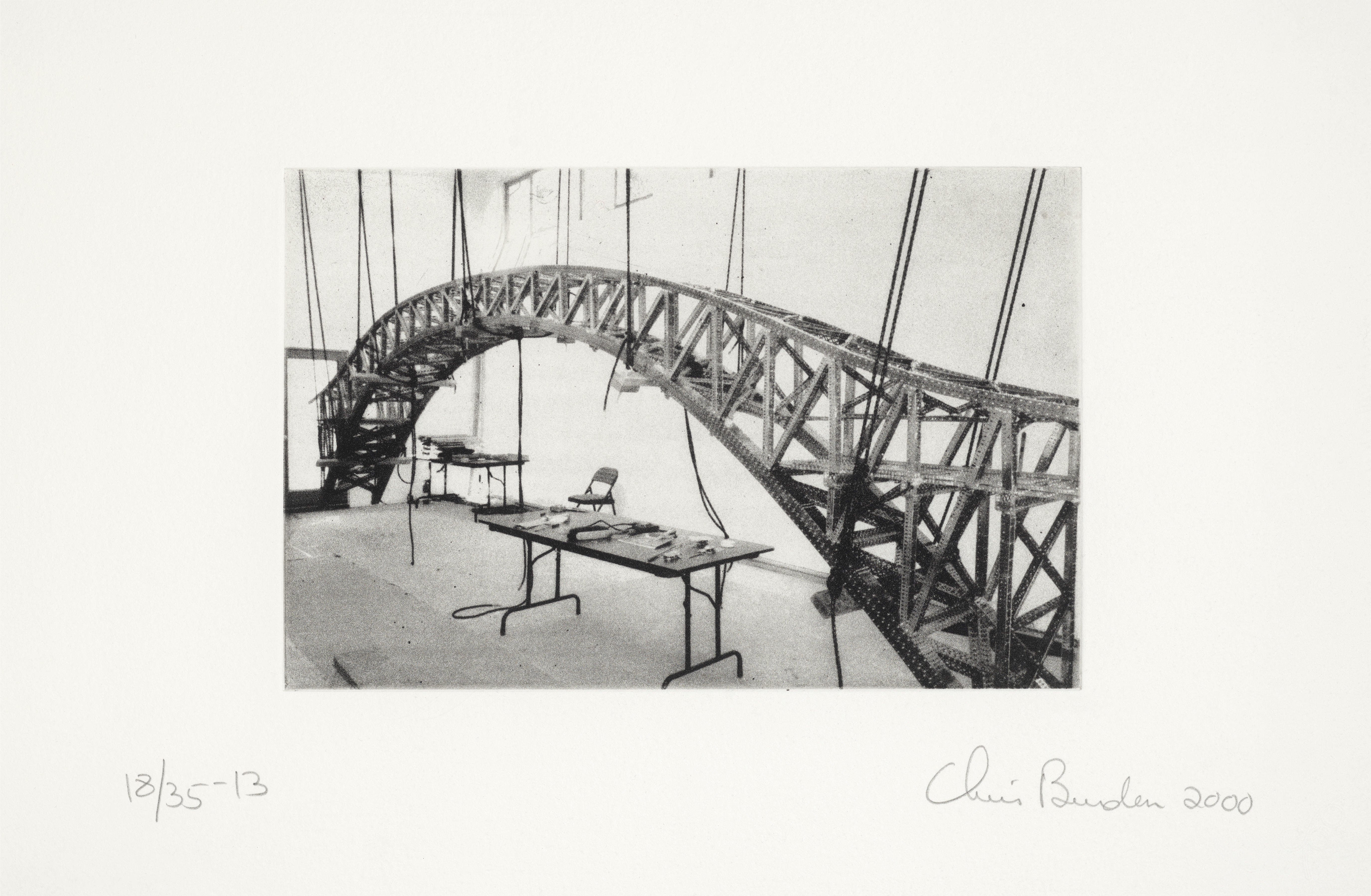 Black and white photograph of a model bridge suspended in a studio.