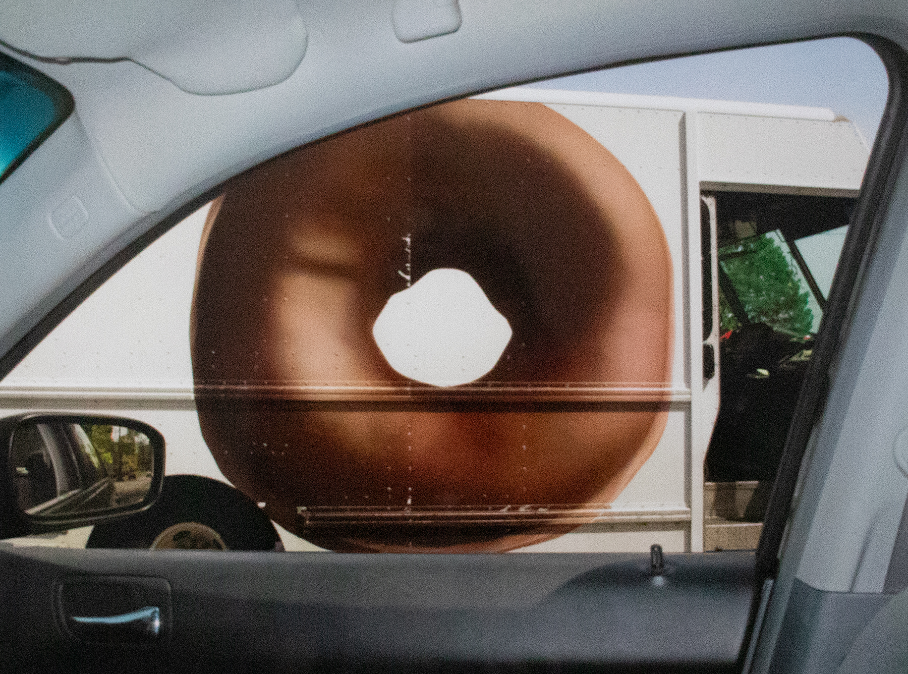 Photograph taken out a passenger side car window of a truck going by with a giant chocolate donut on it.