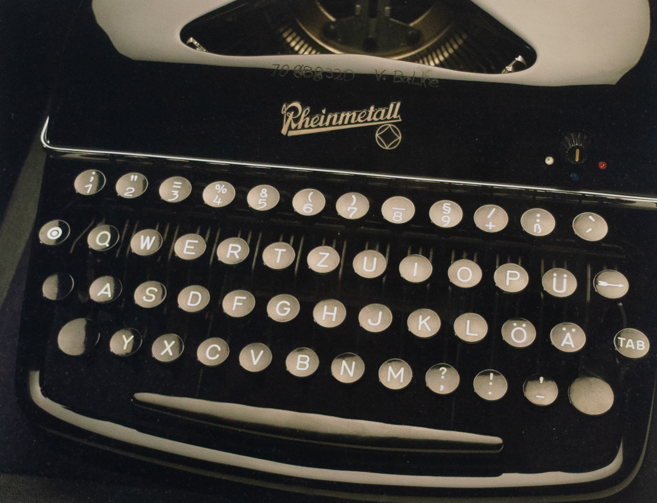 Close up photograph of a black typewriter is pictured with gray keys, carriage and a trademark logo that reads Rheinmetall