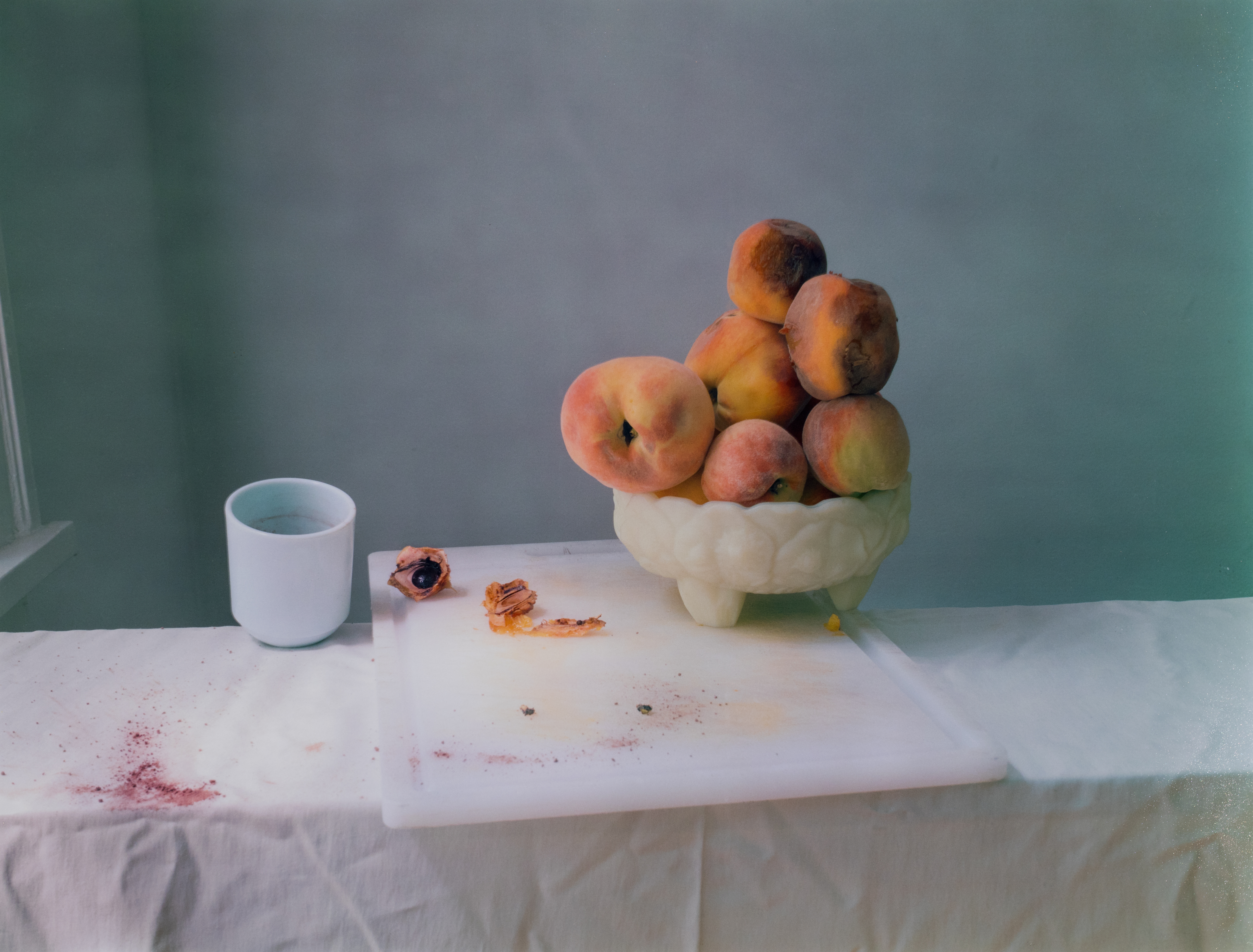White tablecloth with a large cutting board and a bowl overflowing with peaches on top.
