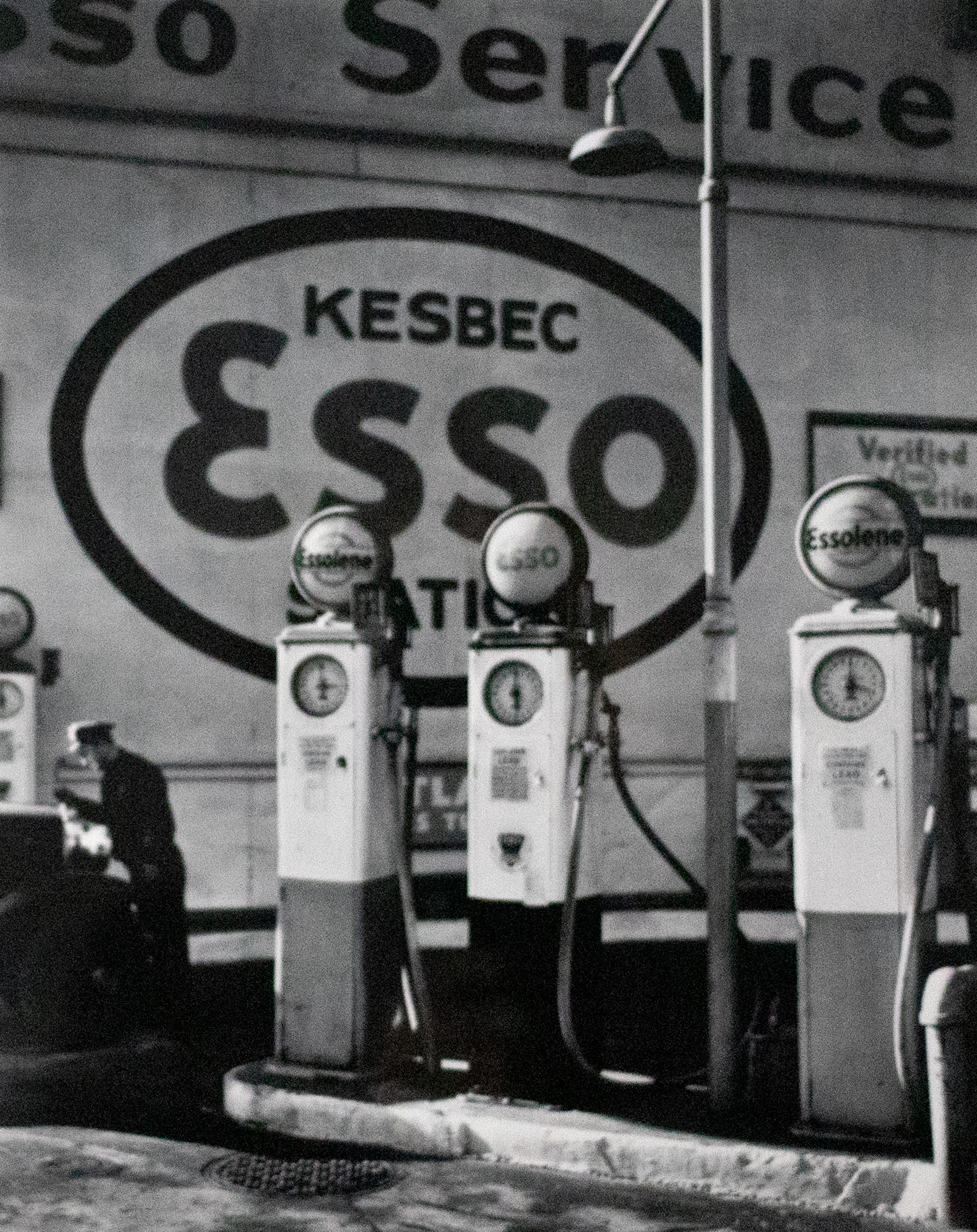 Black and white photograph of three gas pumps and a large sign in the. back that reads &quot;Kesbec Esso&quot;