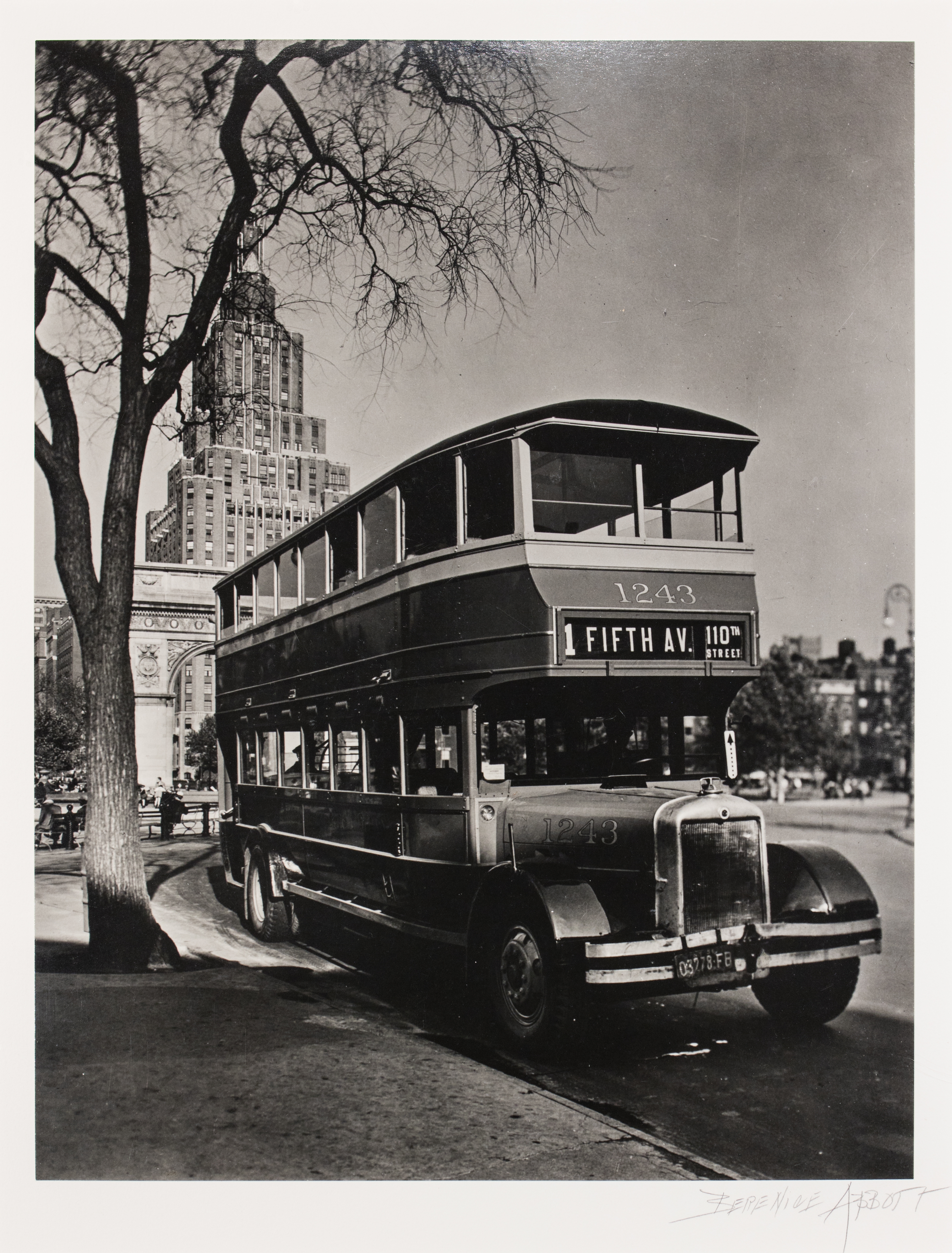 Black and white photograph of an old school double decker bus with New York City buildings in the background.