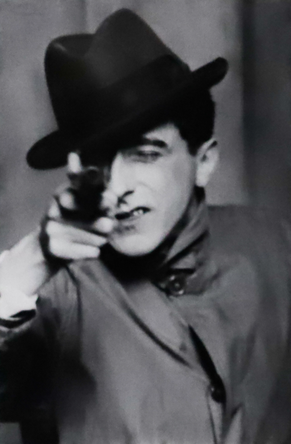 Black and white image of a man in a top hat pointing a gun towards the camera.